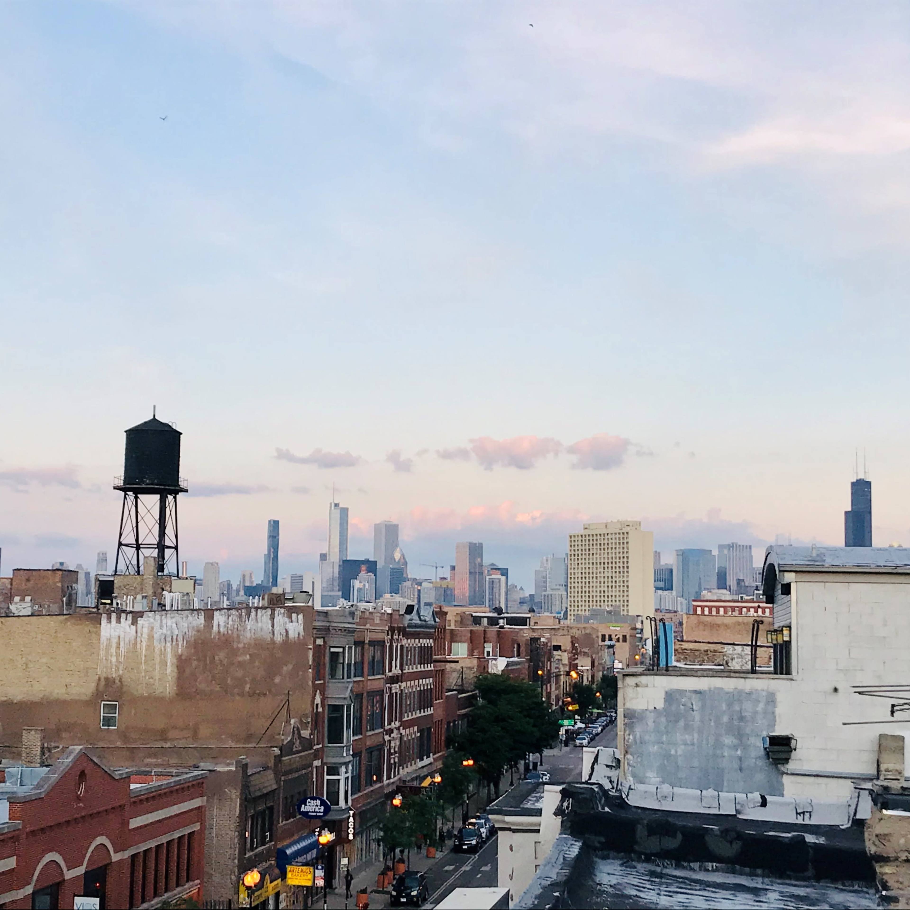 A city skyline with skyscrapers in the background, viewed from a rooftop, along with a water tower and buildings in the foreground.