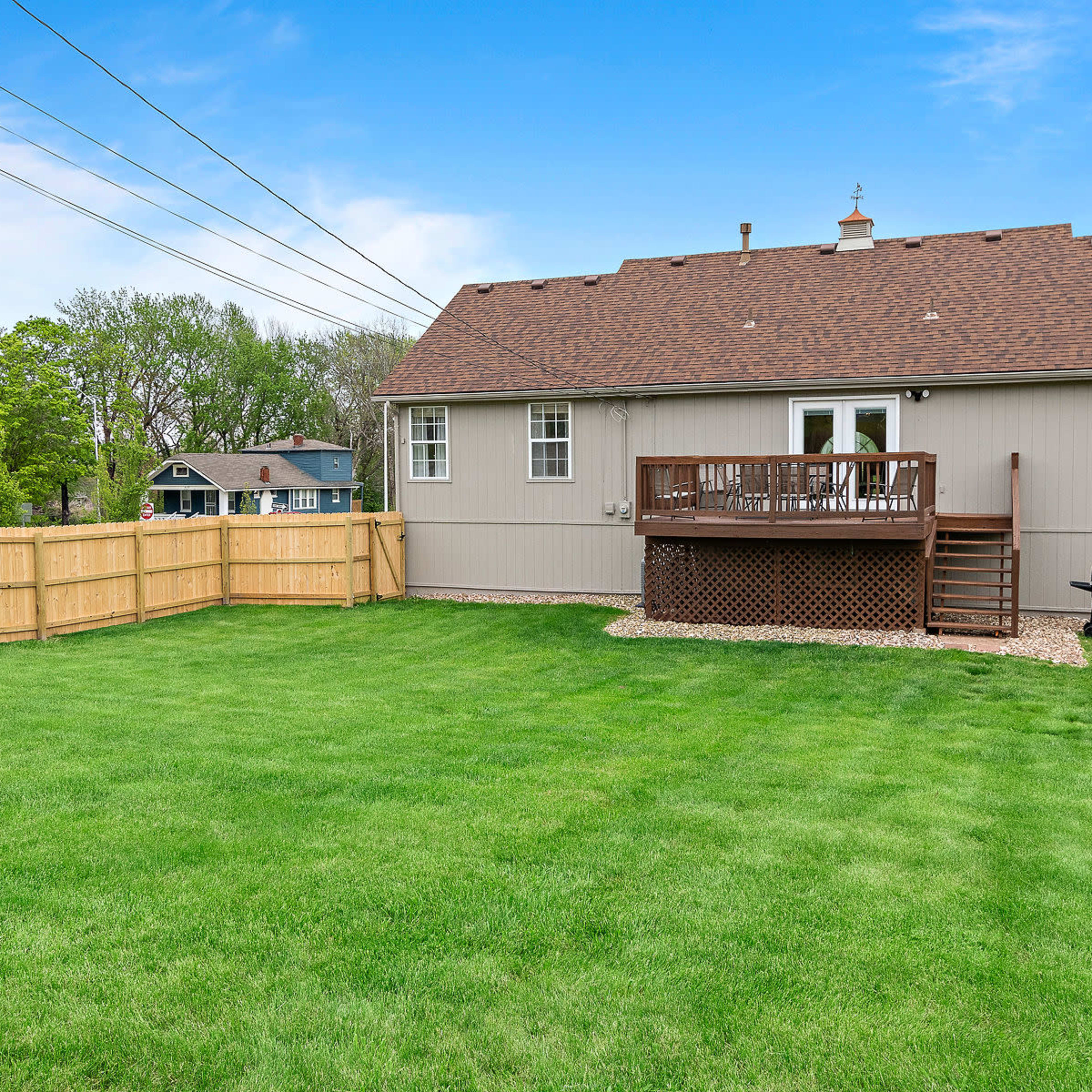 A fenced backyard with a well-manicured lawn and a two-story house featuring a deck and a barbecue grill.