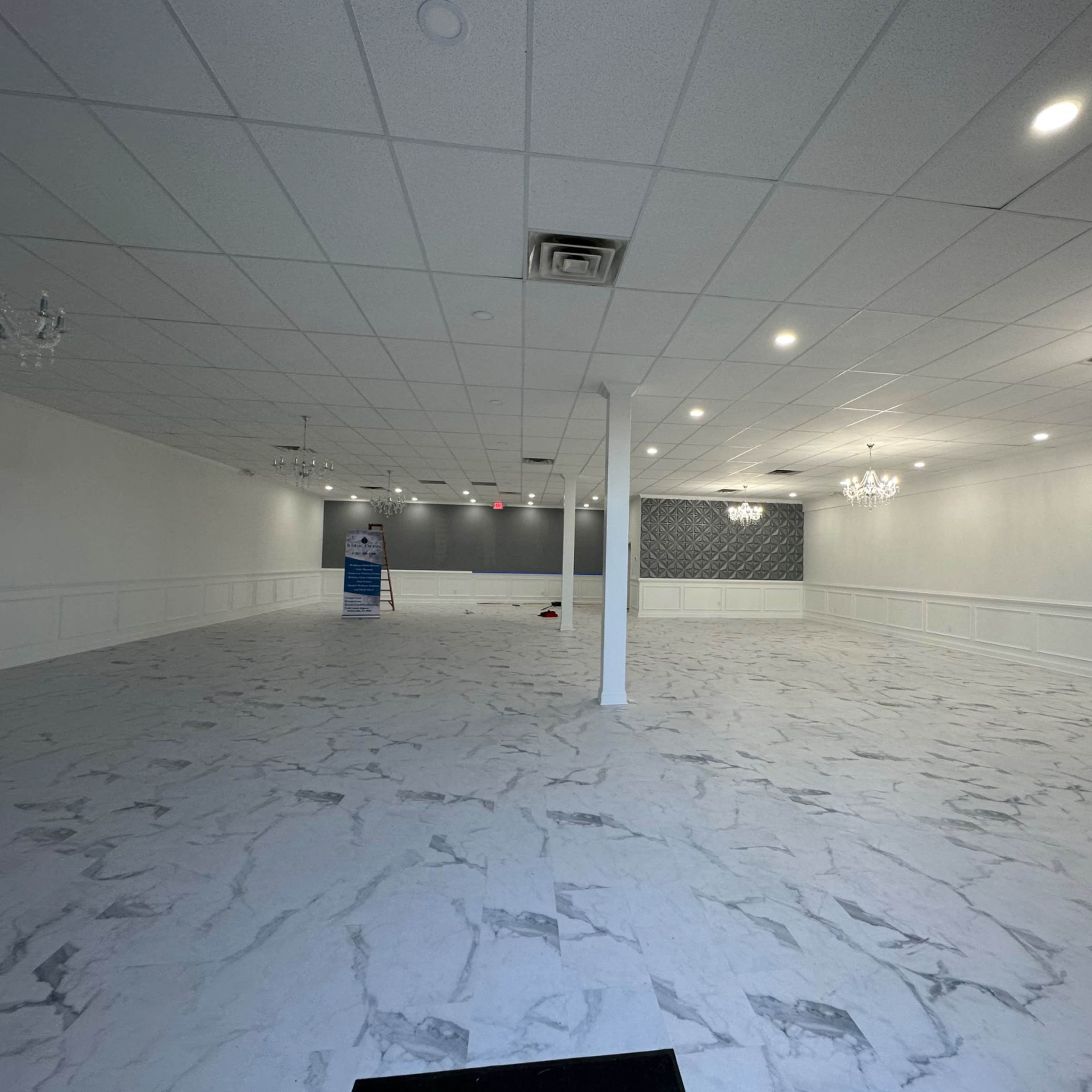 A spacious, empty room featuring a marble-patterned floor, white walls, and several chandeliers hanging from the ceiling.