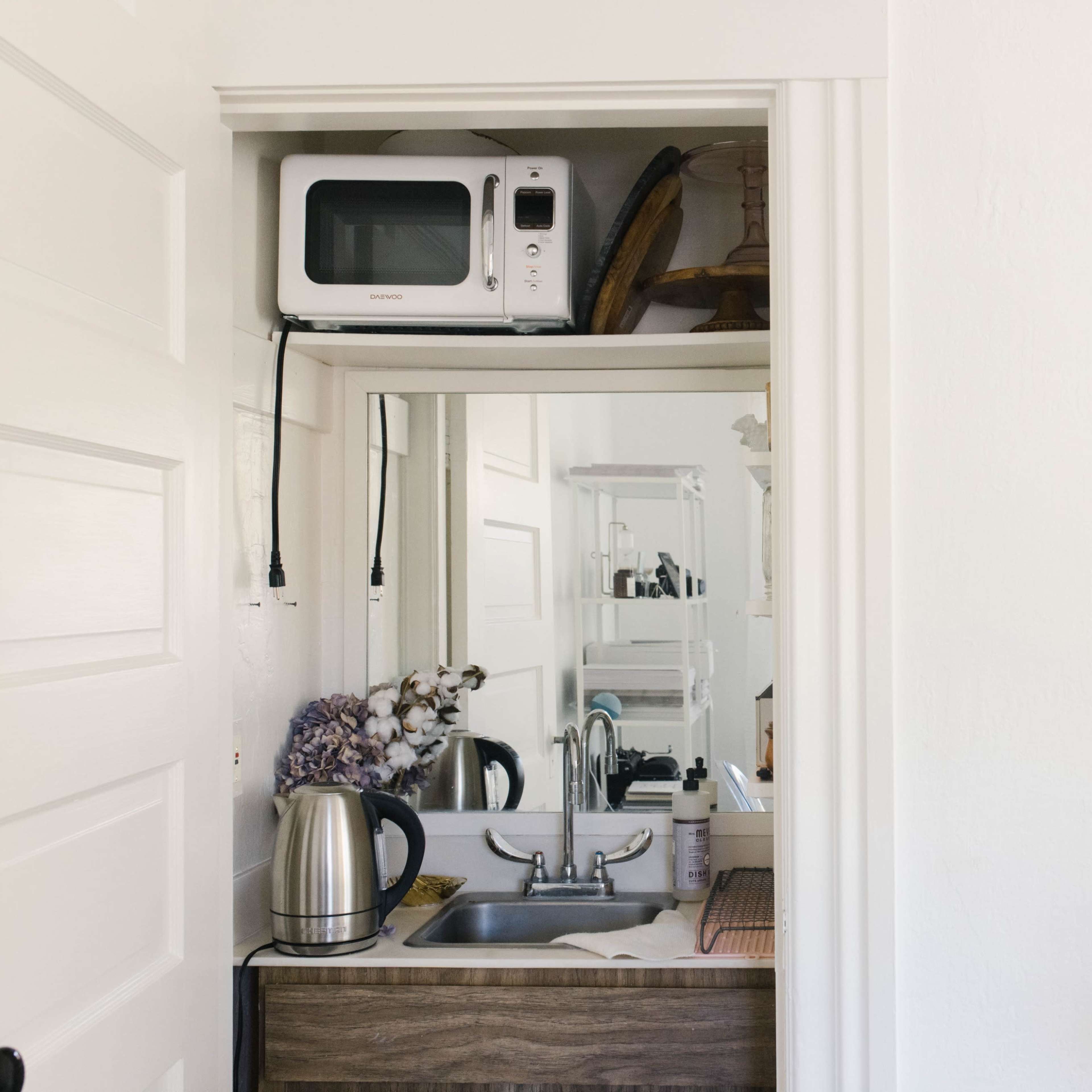 A small kitchenette area features a microwave and a kettle above a sink, with minimal decor on the shelves.