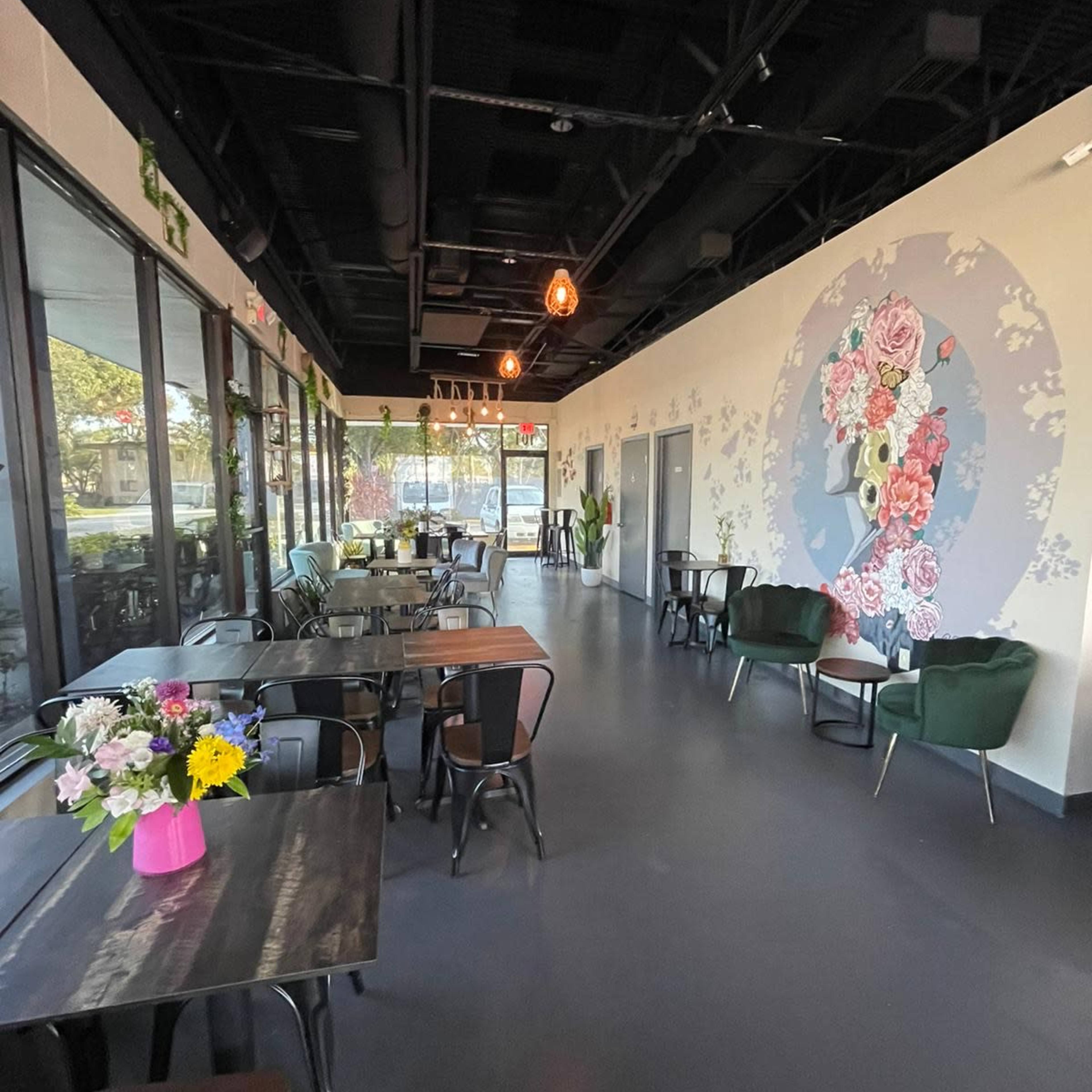 The interior of a modern café featuring tables, chairs, and a mural with floral designs on one wall.