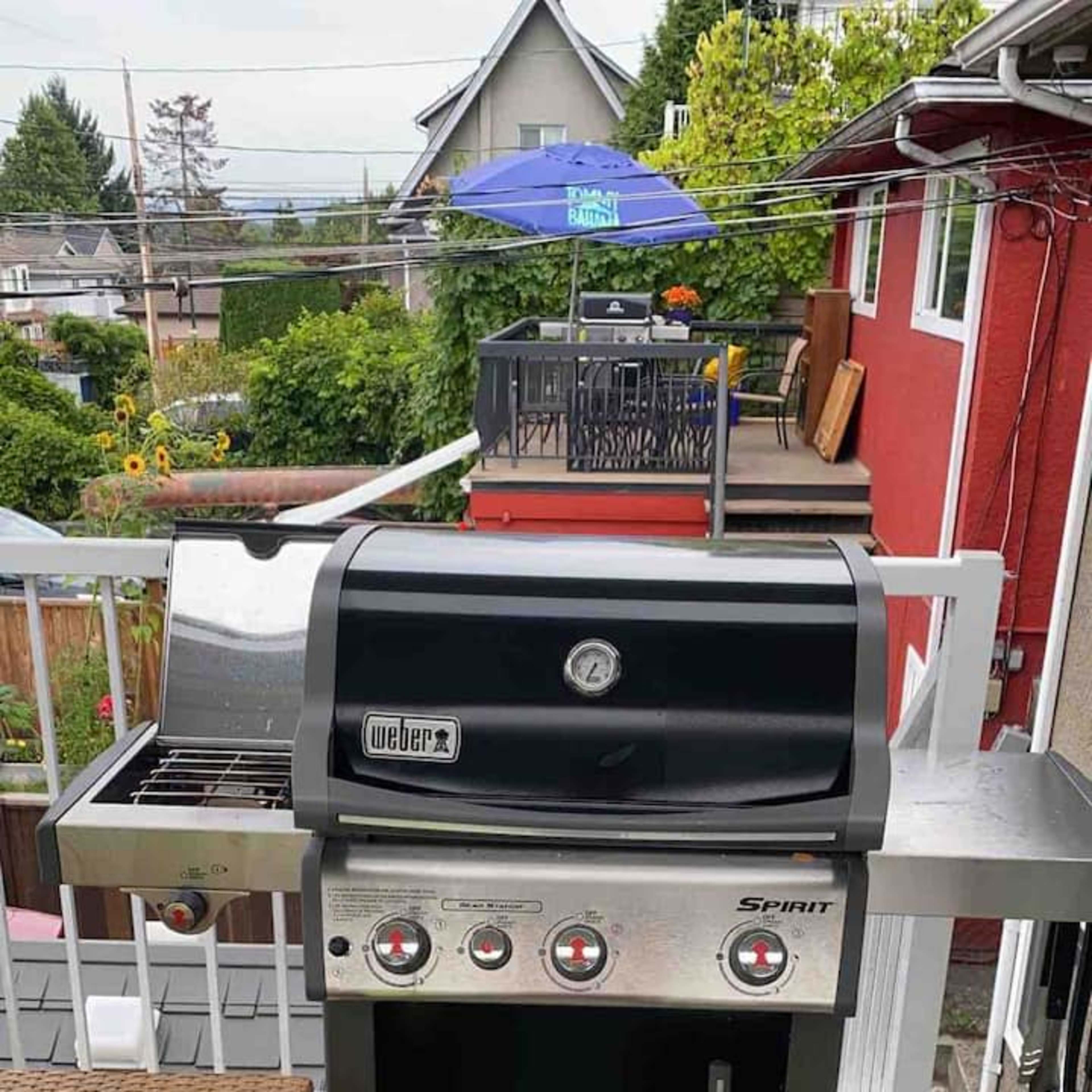 A black Weber gas grill placed on a patio with outdoor furniture and a dining area in the background.