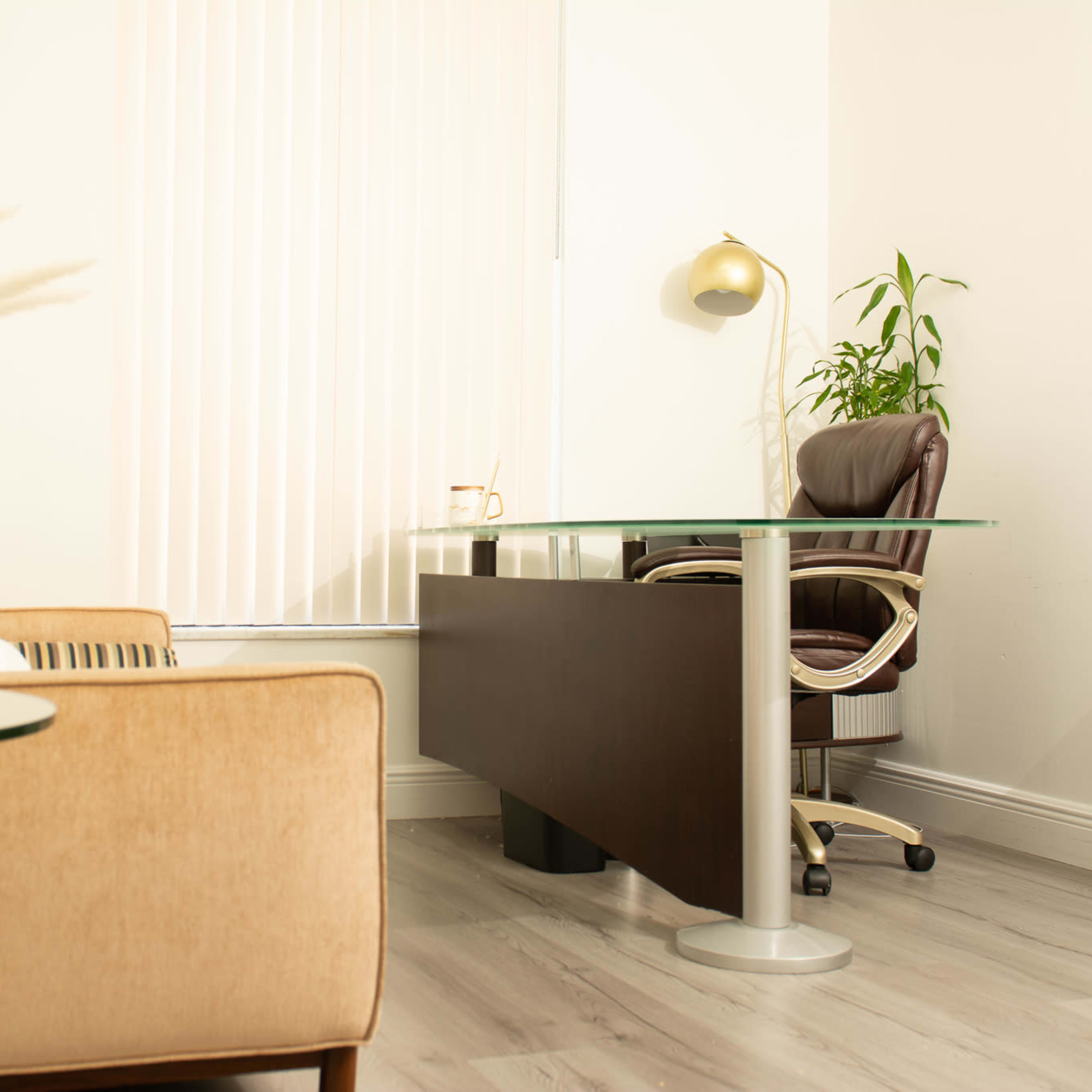A modern office space with a large desk, a comfortable chair, a potted plant, and a seating area with a sofa and a side table.