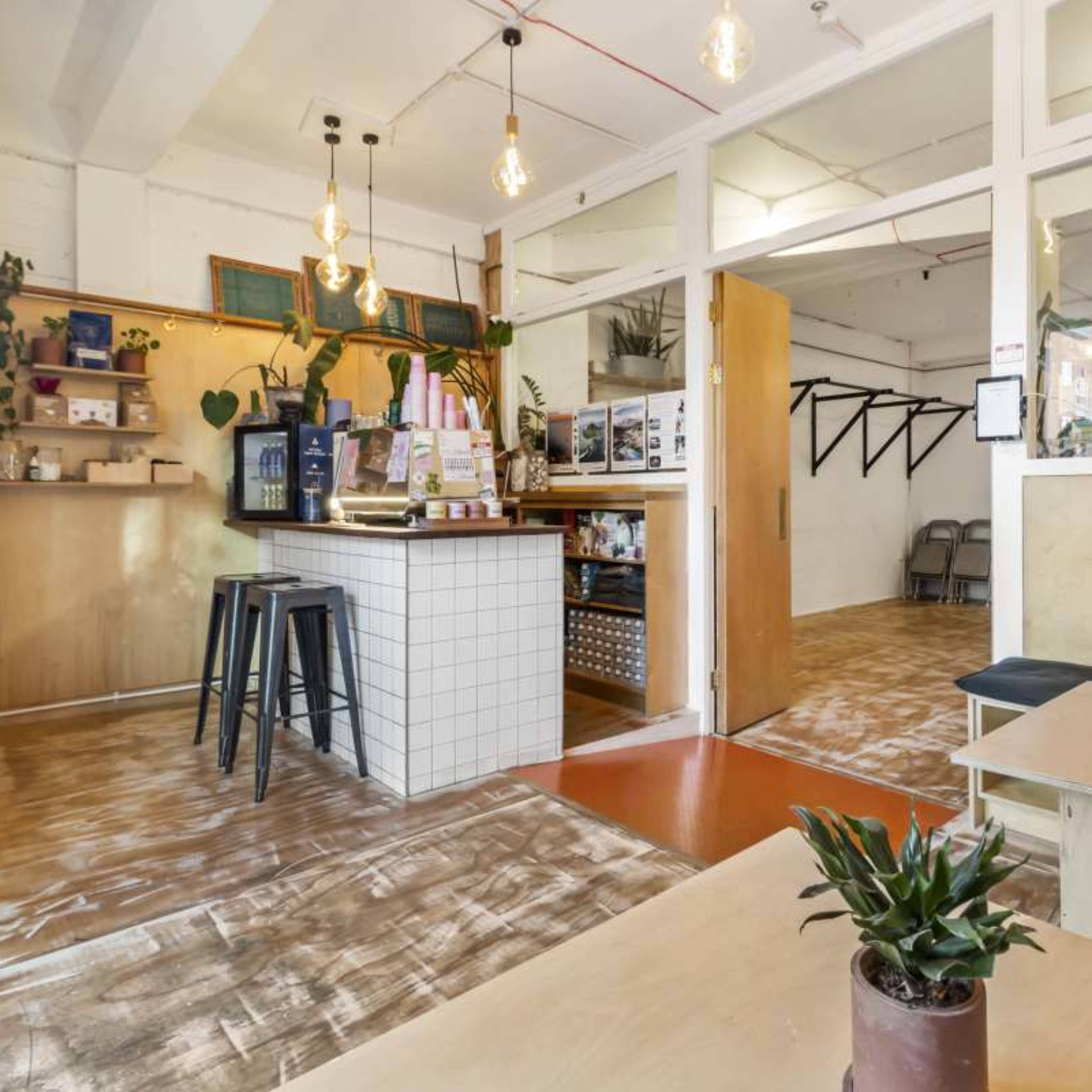 A modern cafe interior with a bar counter, wooden tables, and plants decorating the space.