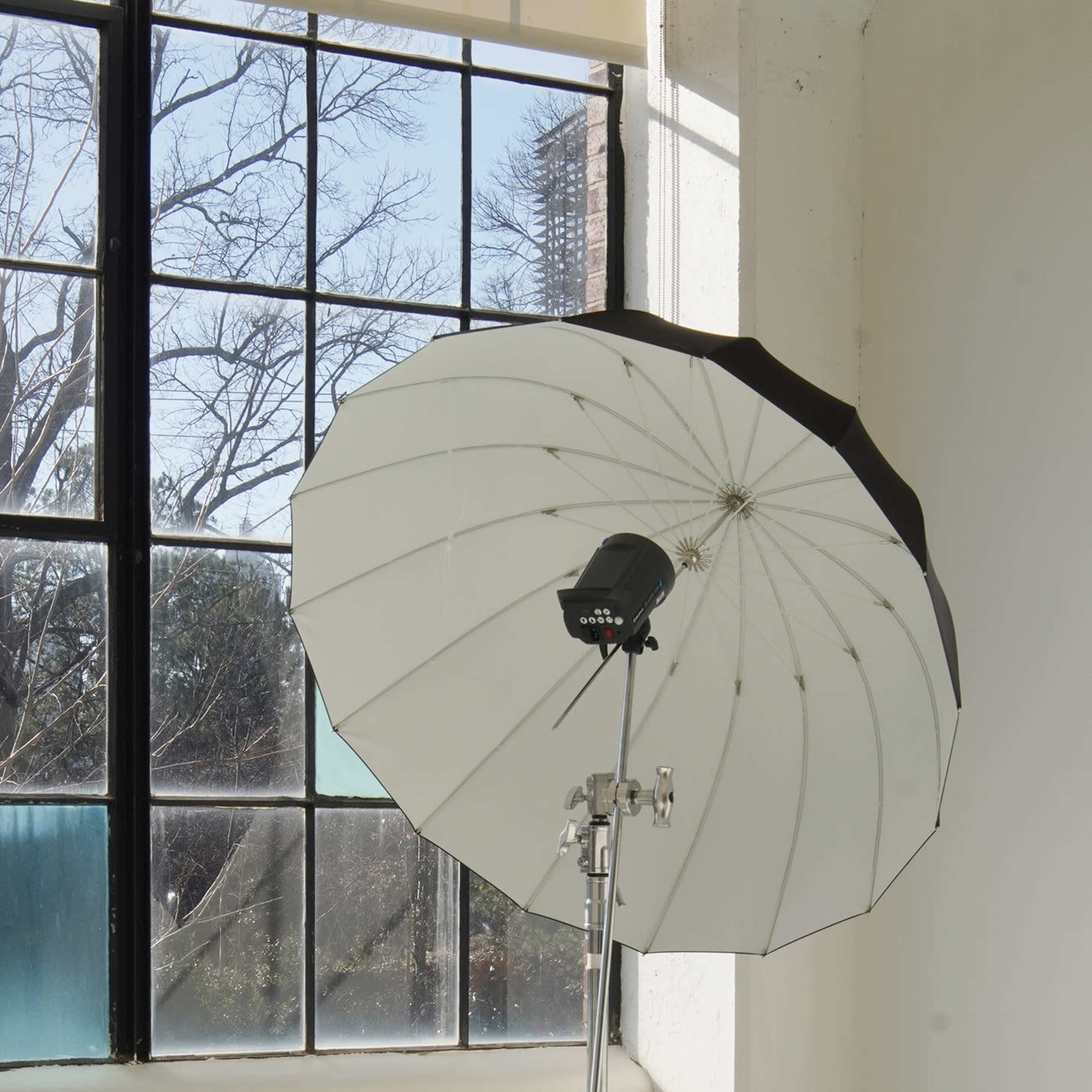 A reflective umbrella is mounted on a metal stand in a room with large windows.