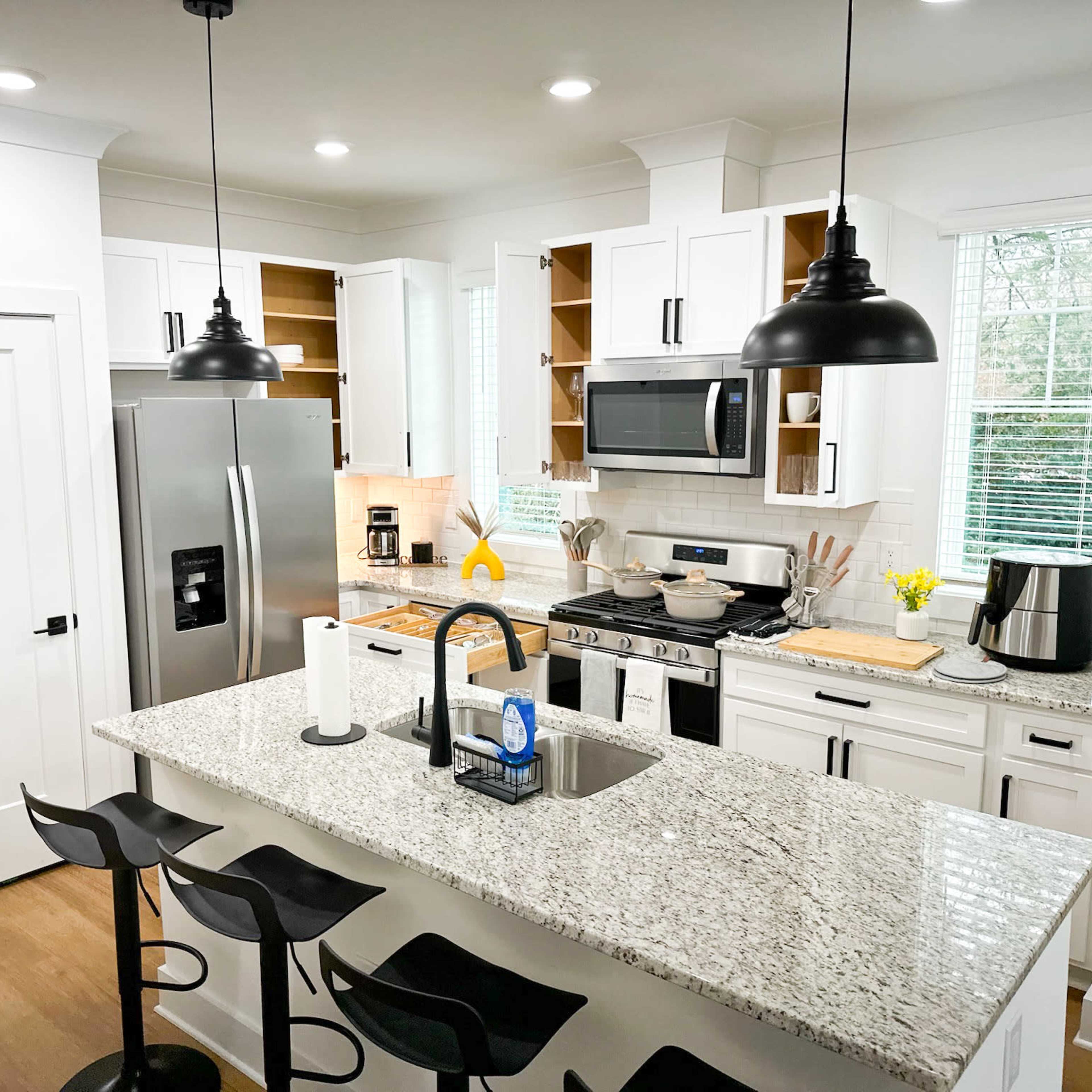 A modern kitchen features white cabinets, stainless steel appliances, and a large granite island with bar stools.