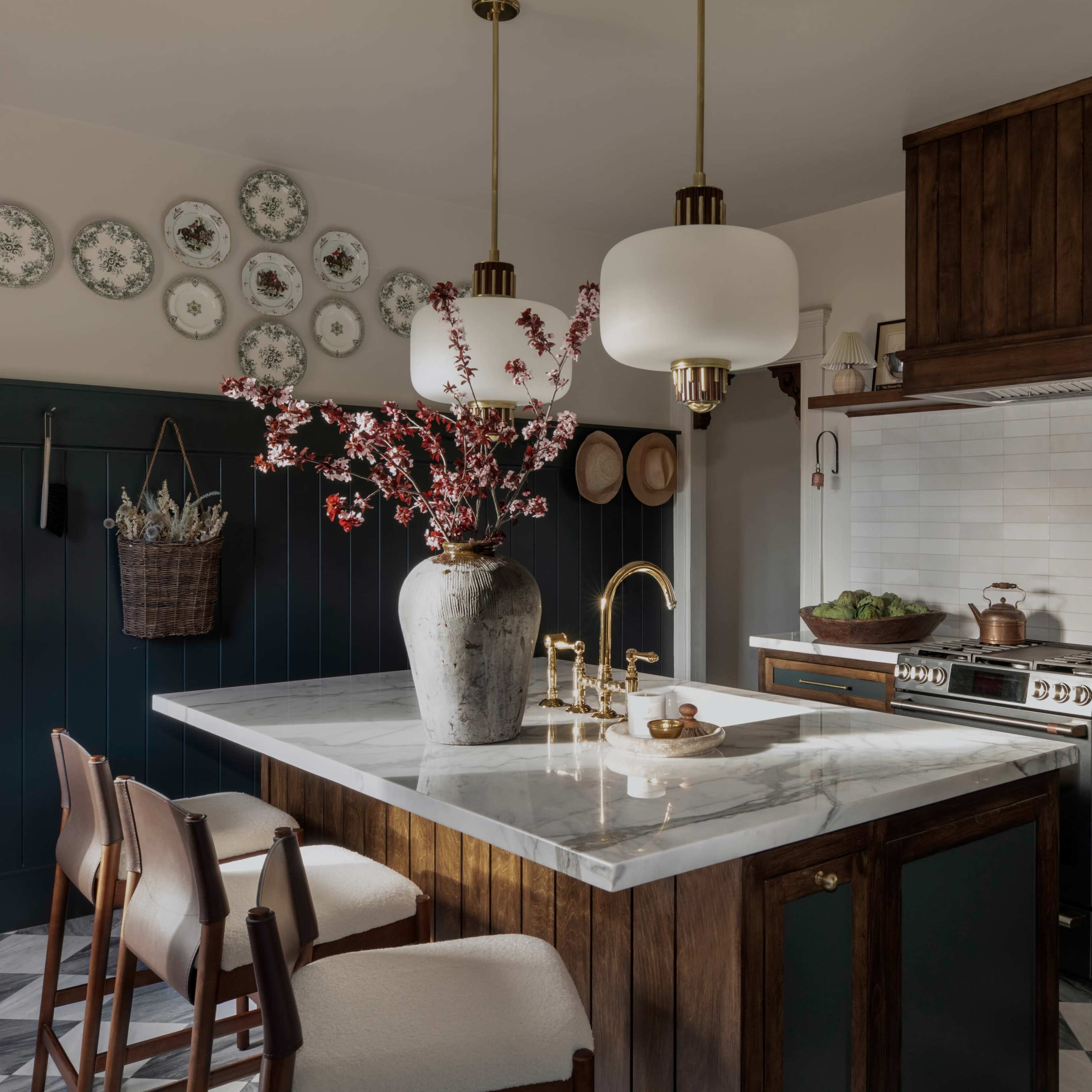 A modern kitchen features a central marble island, wooden cabinetry, and decorative plates on the wall.