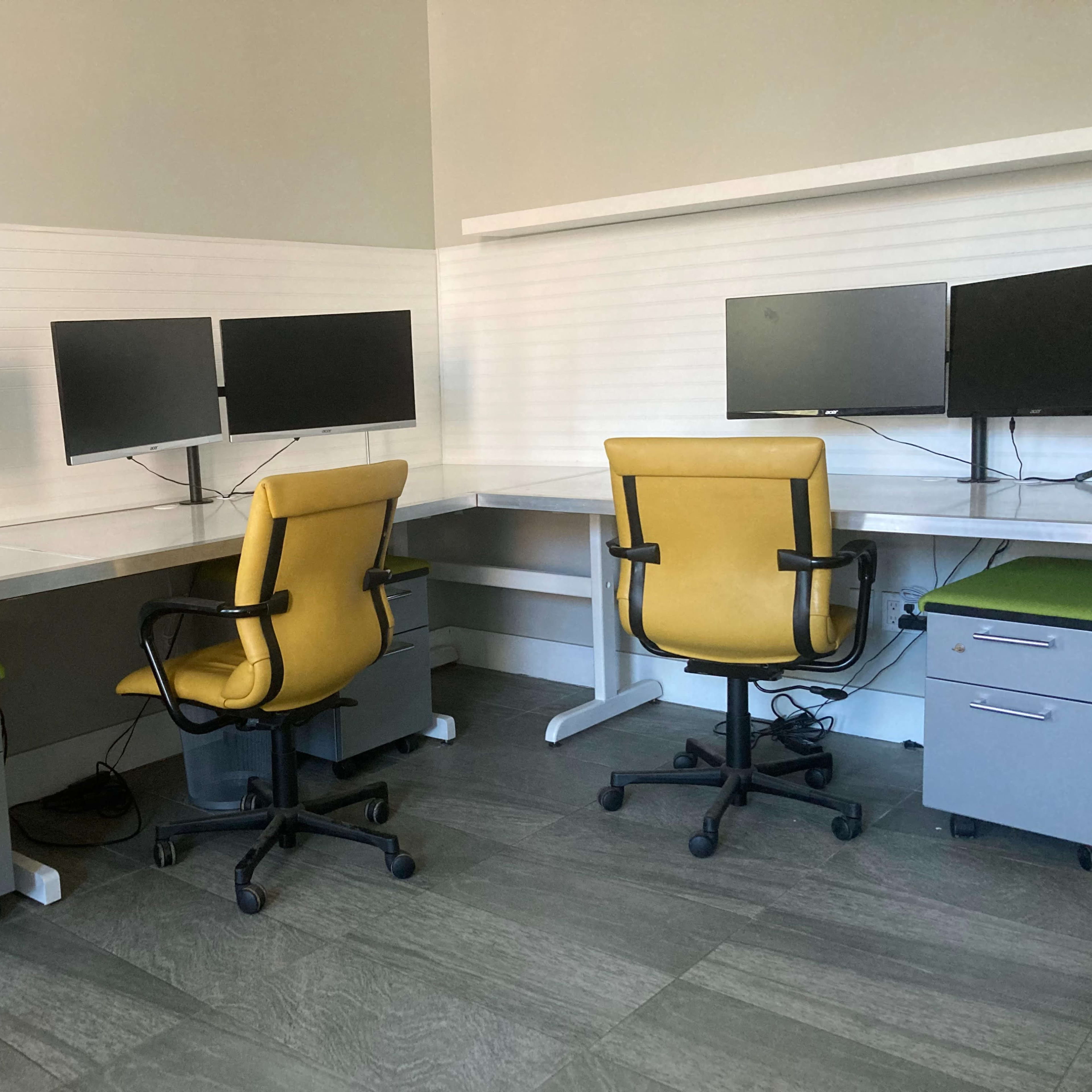 A workspace featuring two yellow office chairs and four computer monitors arranged on white desks.