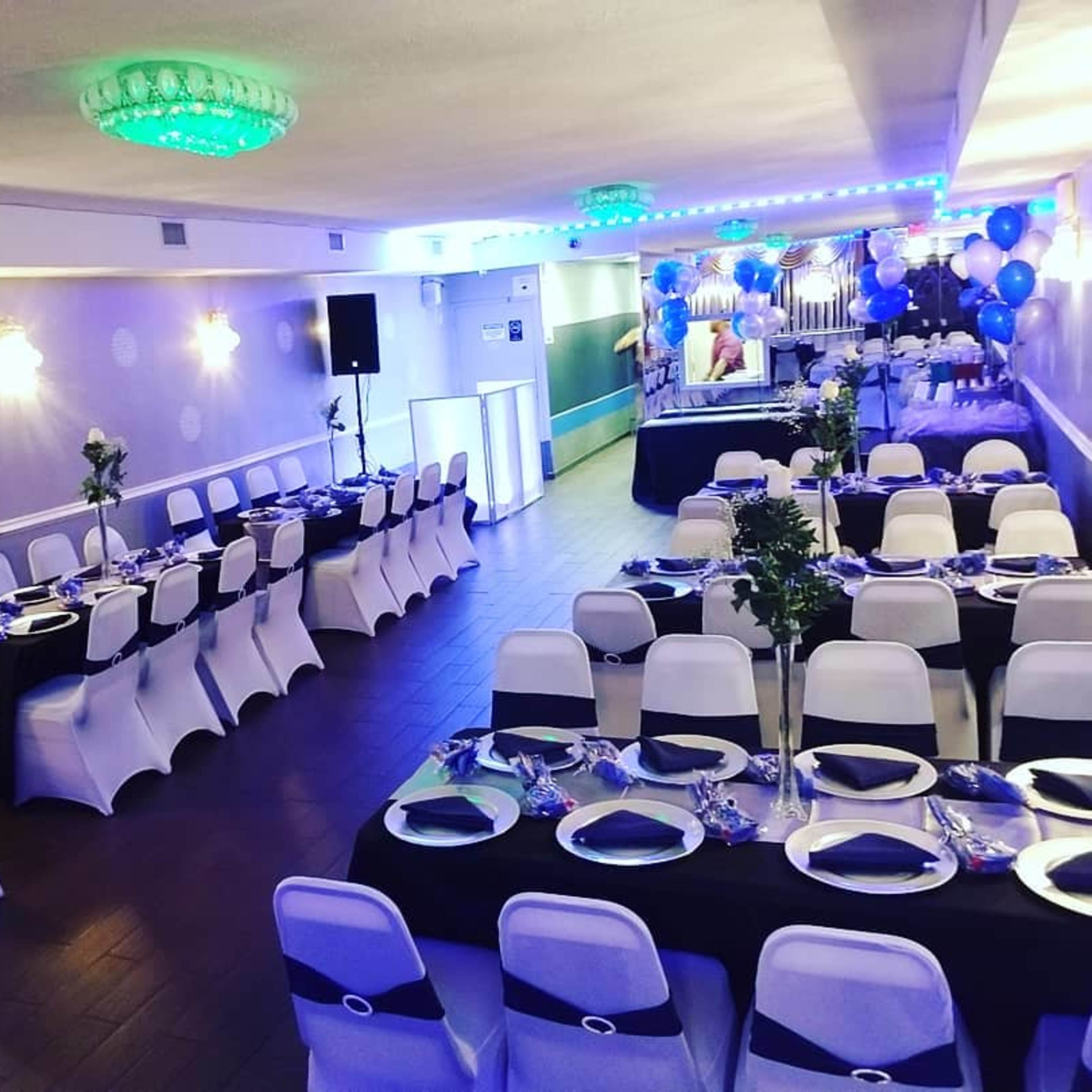 A decorated event space with rows of tables, white chairs, and blue balloons arranged for a gathering.