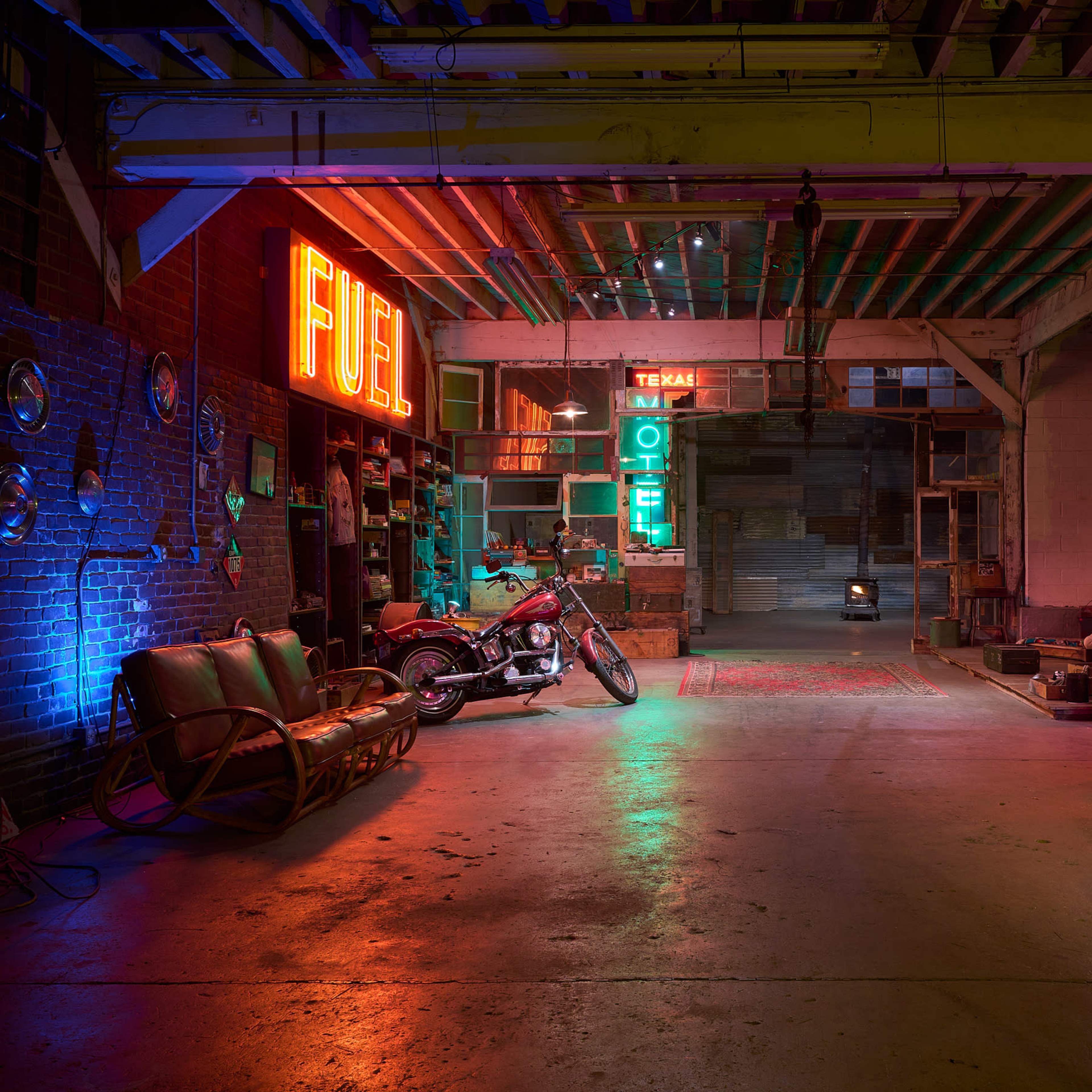 A dimly lit garage or workshop with colorful neon signs, a motorcycle parked to one side, and various artifacts and furniture arranged around the space.