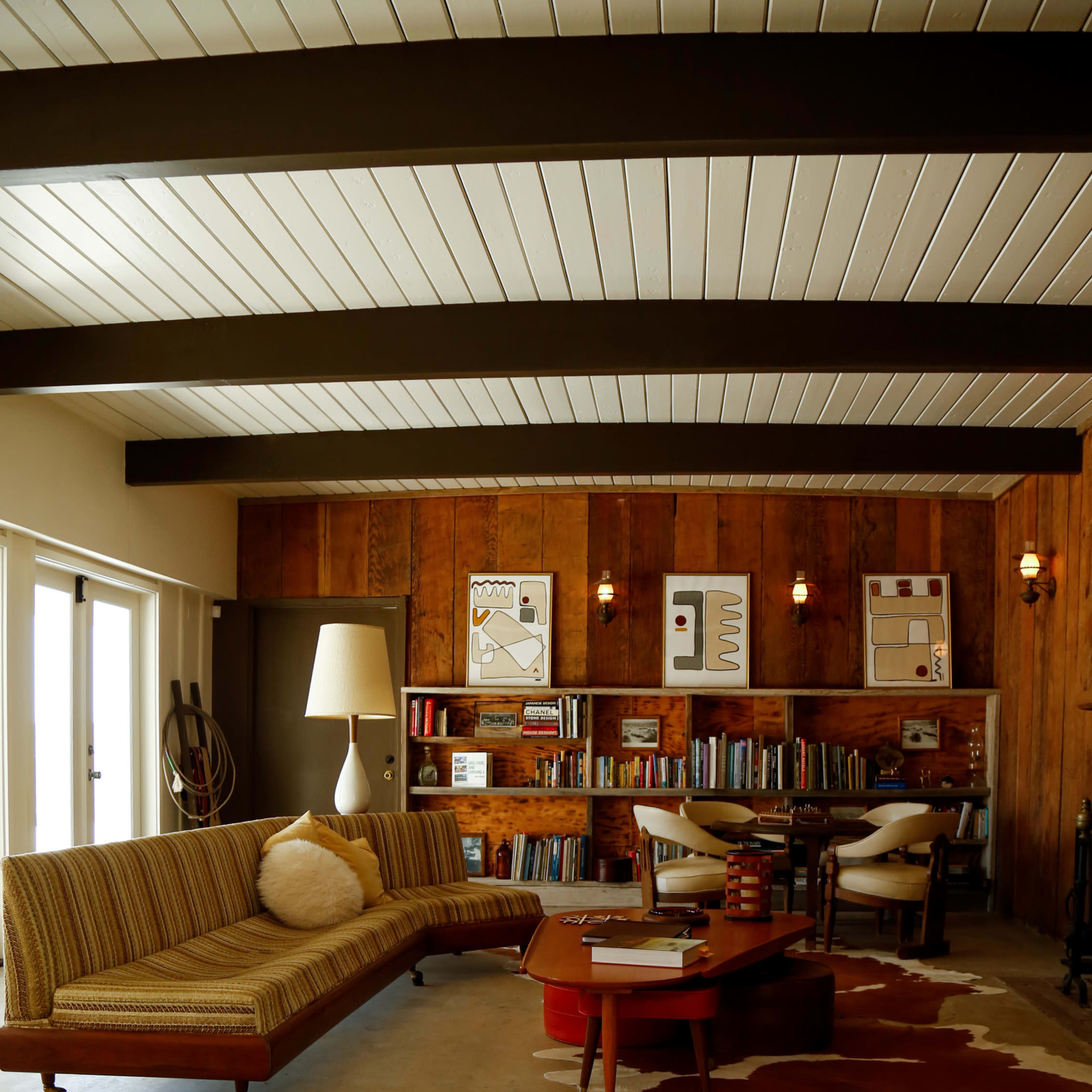 A mid-century modern living room featuring a striped sofa, a wooden bookshelf filled with books, and a cowhide rug on a polished concrete floor.