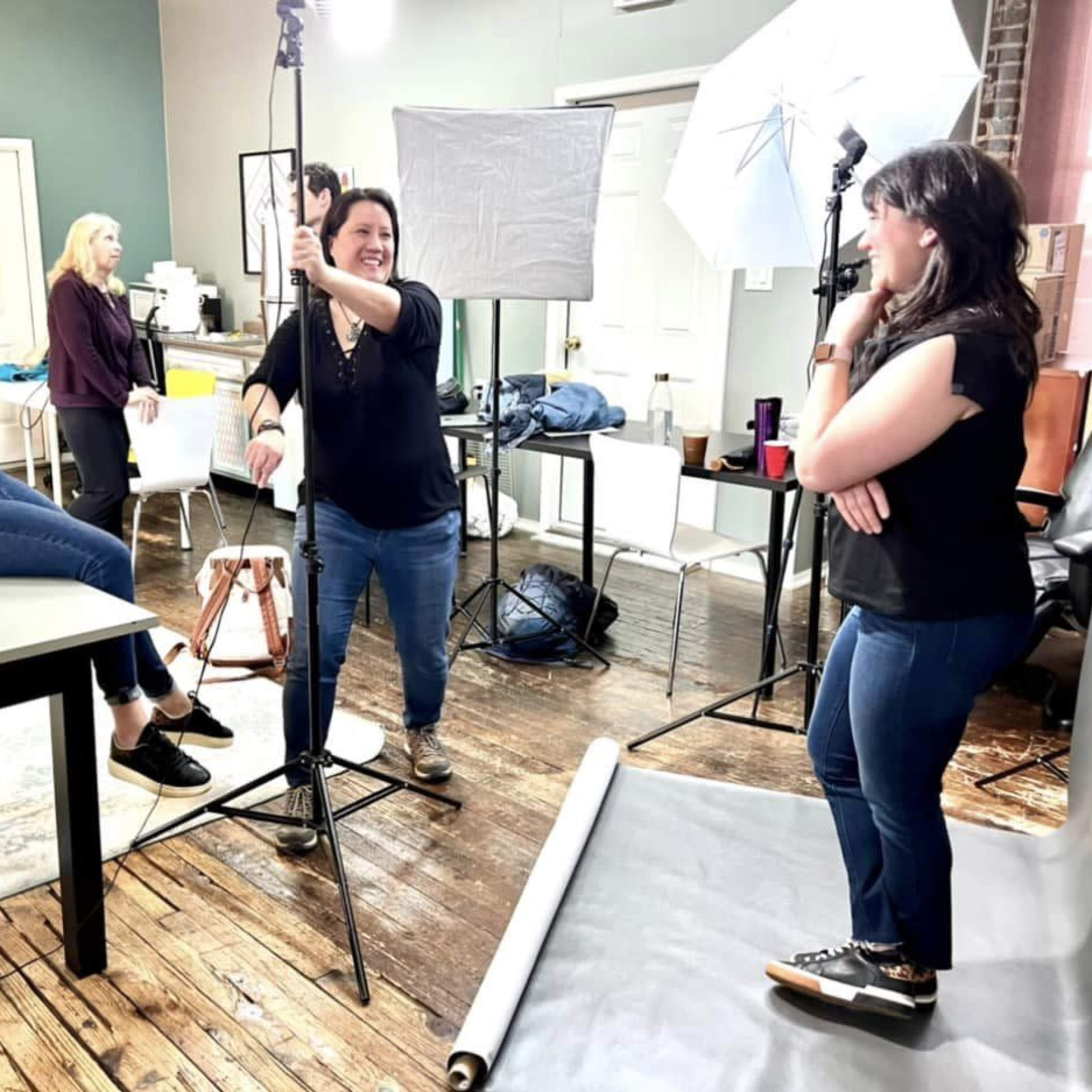 A group of photographers and their subject interact during a photo shoot in a studio setting.