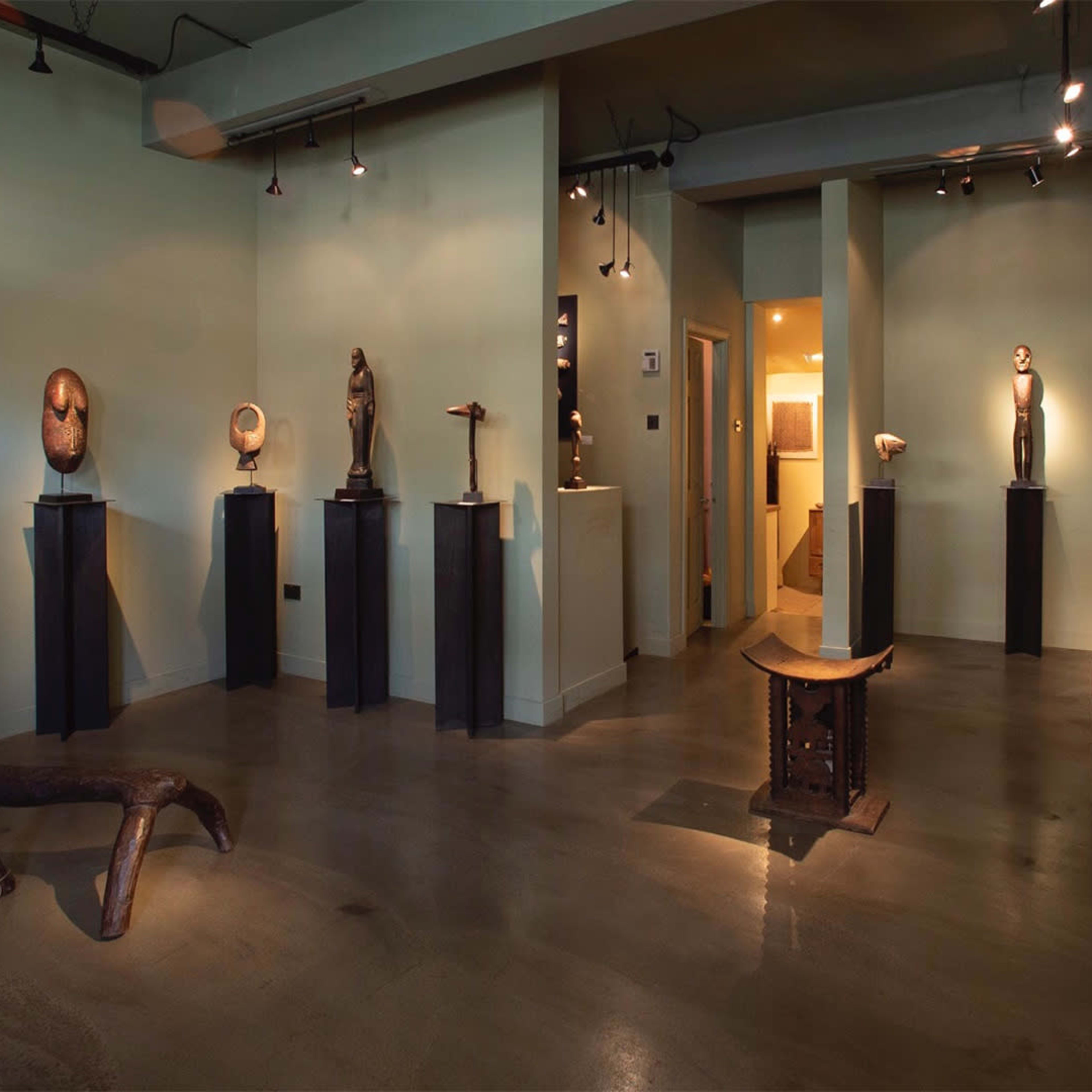 An art gallery featuring a variety of sculptures displayed on pedestals within a green-walled space.