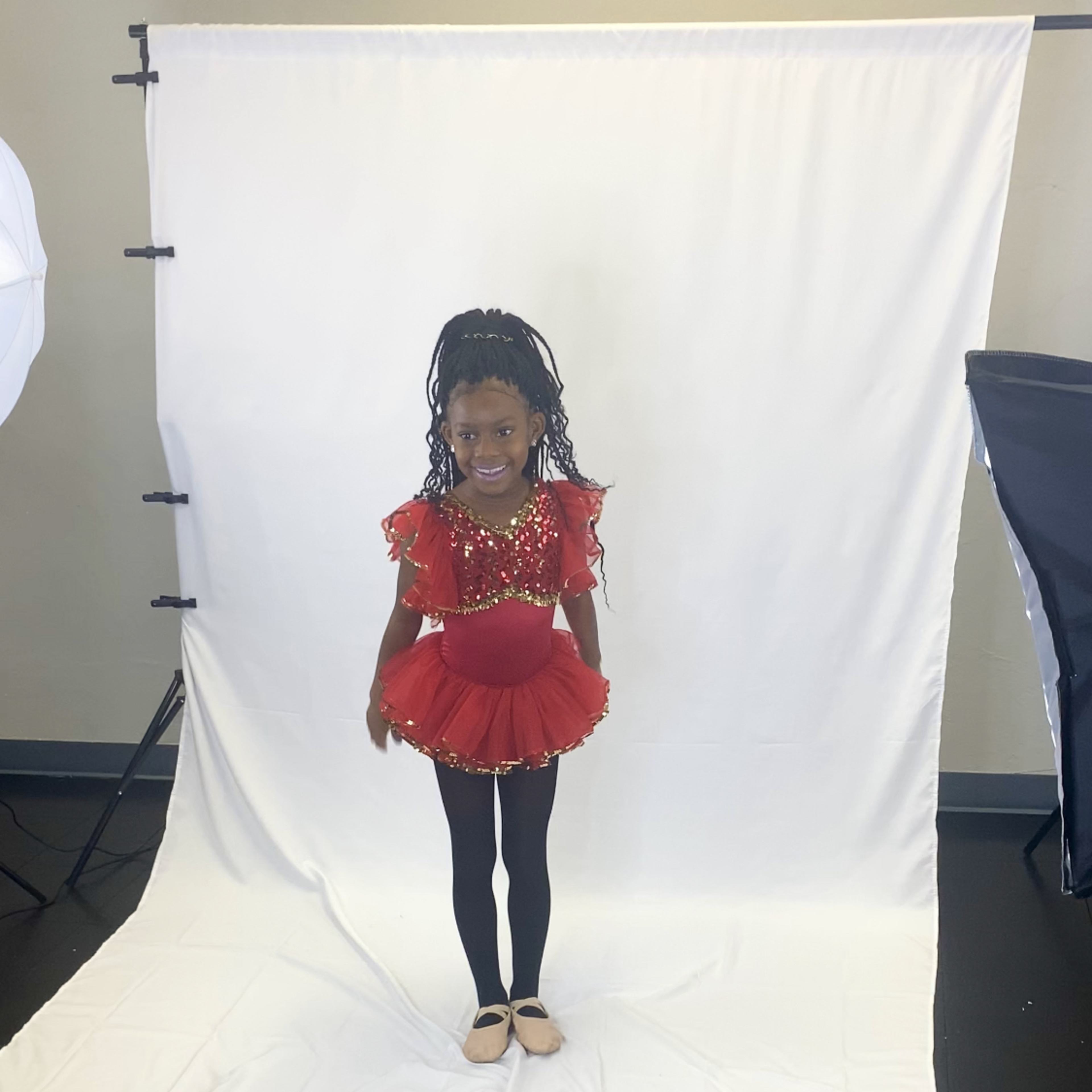 A young girl in a red sequined dance costume poses in front of a white backdrop.