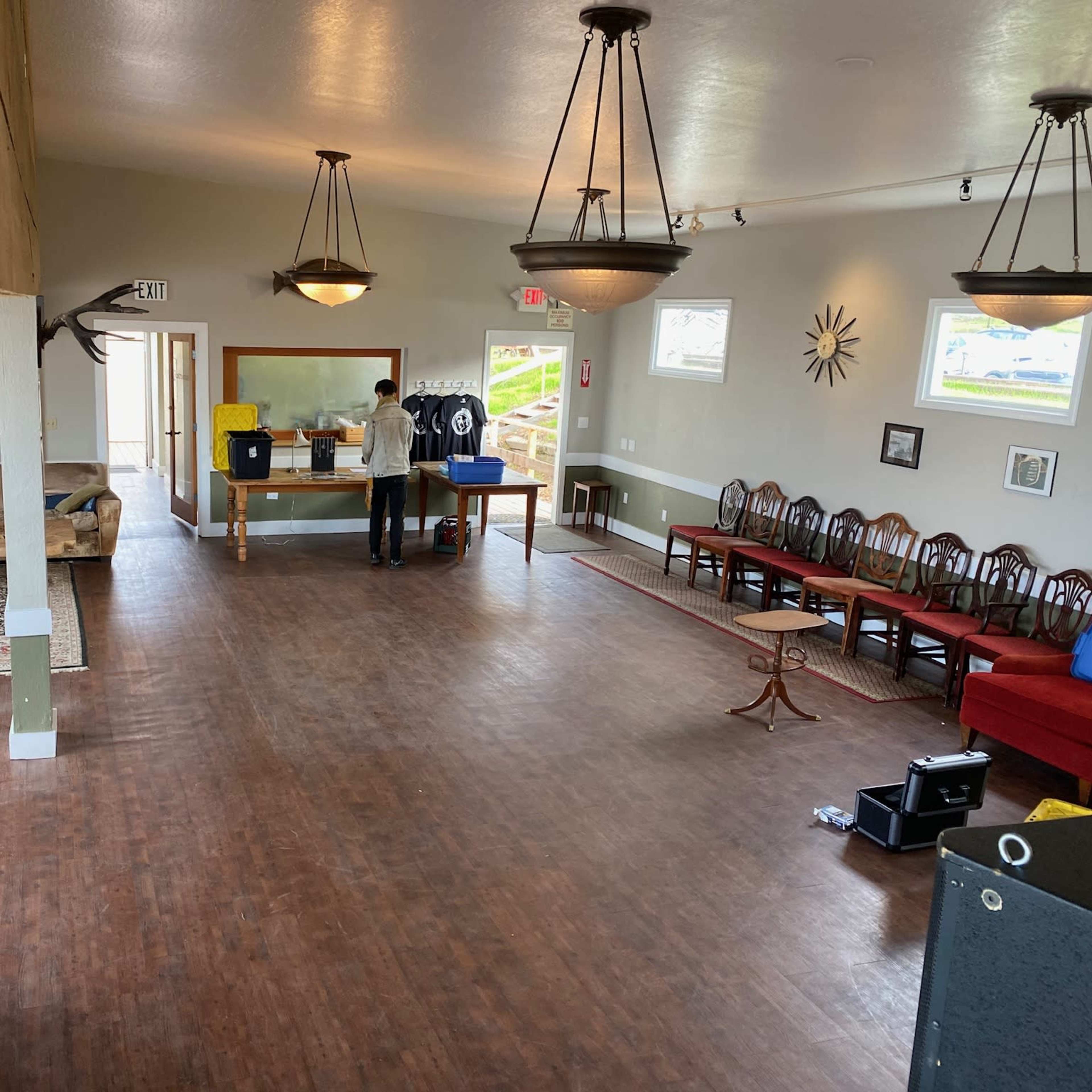 The interior of a spacious community room features a seating area with sofas, a serving counter, and a few people engaging in activities.