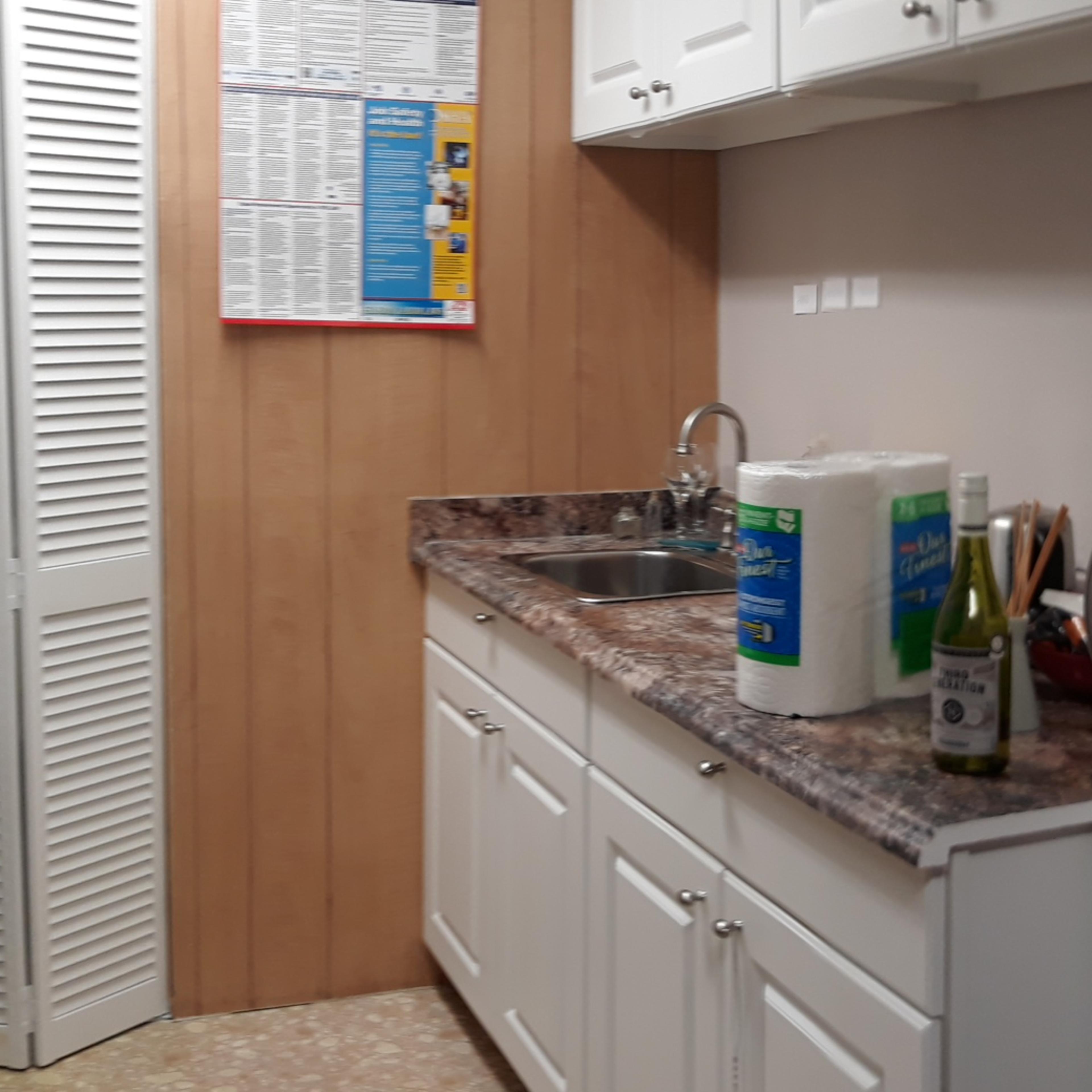 A kitchen area featuring white cabinets, a sink, a granite countertop, and a closet with louvered doors.