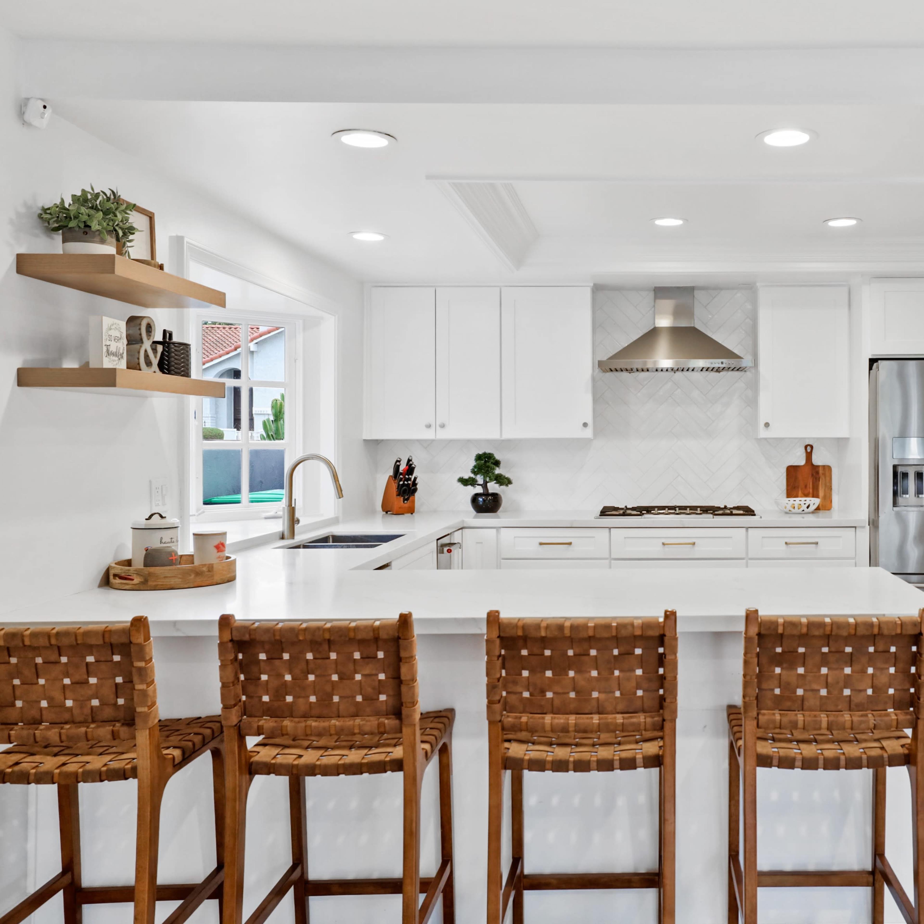 A modern kitchen featuring white cabinetry, a central island with four woven bar stools, and stainless steel appliances.