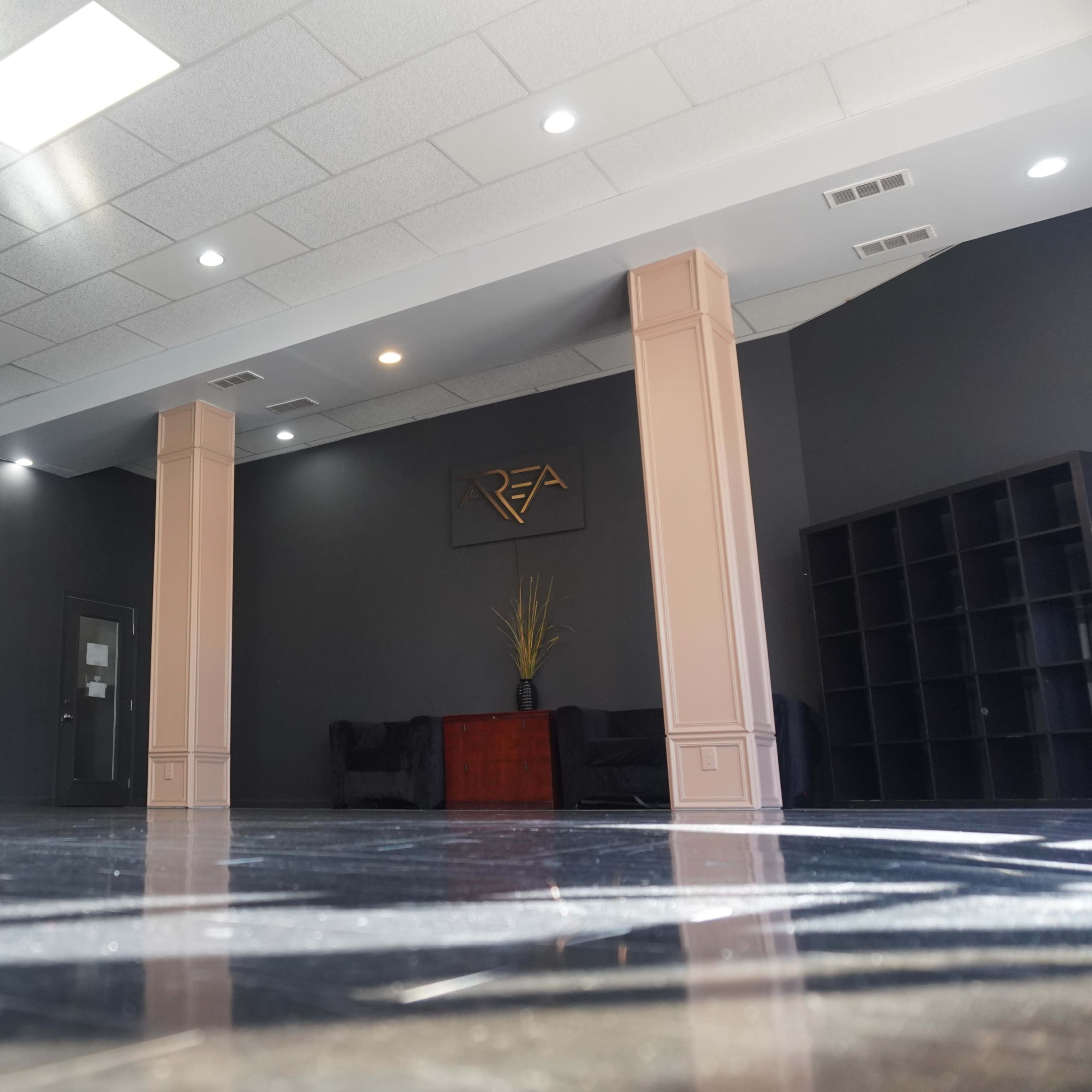 An empty room with dark gray walls, polished flooring, and two light-colored columns, featuring a seating area and a wall shelf.