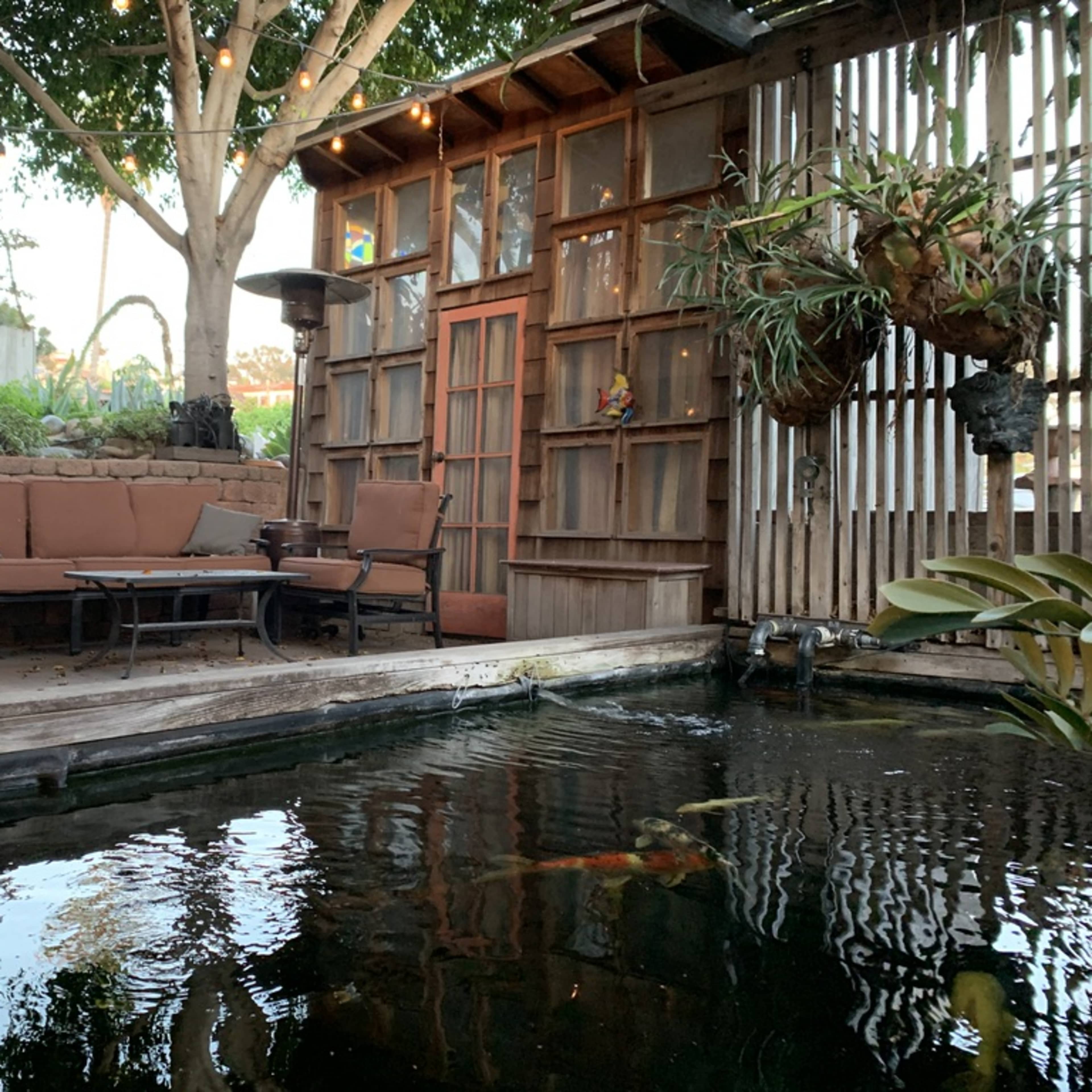 A cozy outdoor seating area beside a koi pond, surrounded by plants and wooden structures.