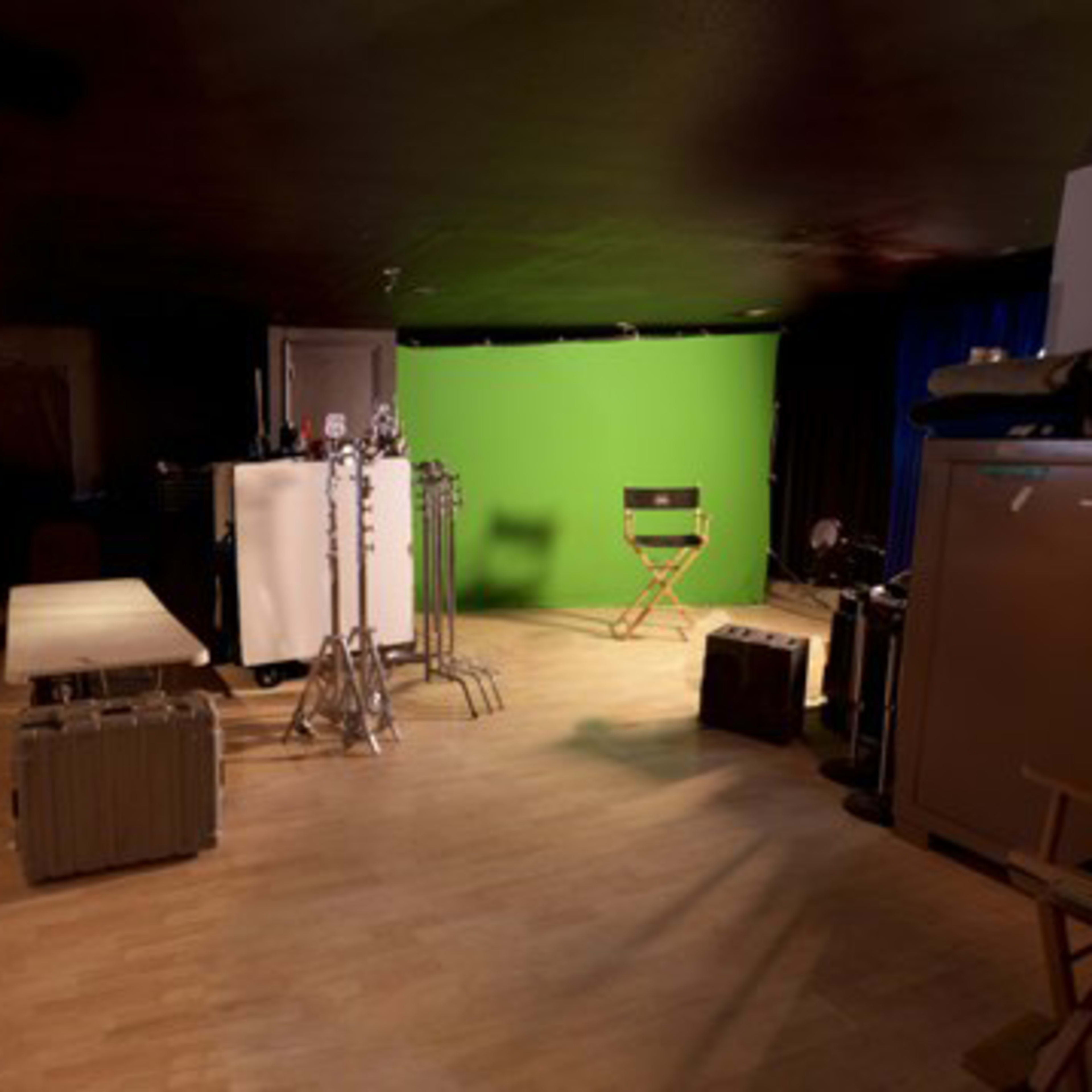 A room with storage shelves filled with equipment cases, a green screen setup, and a director's chair.
