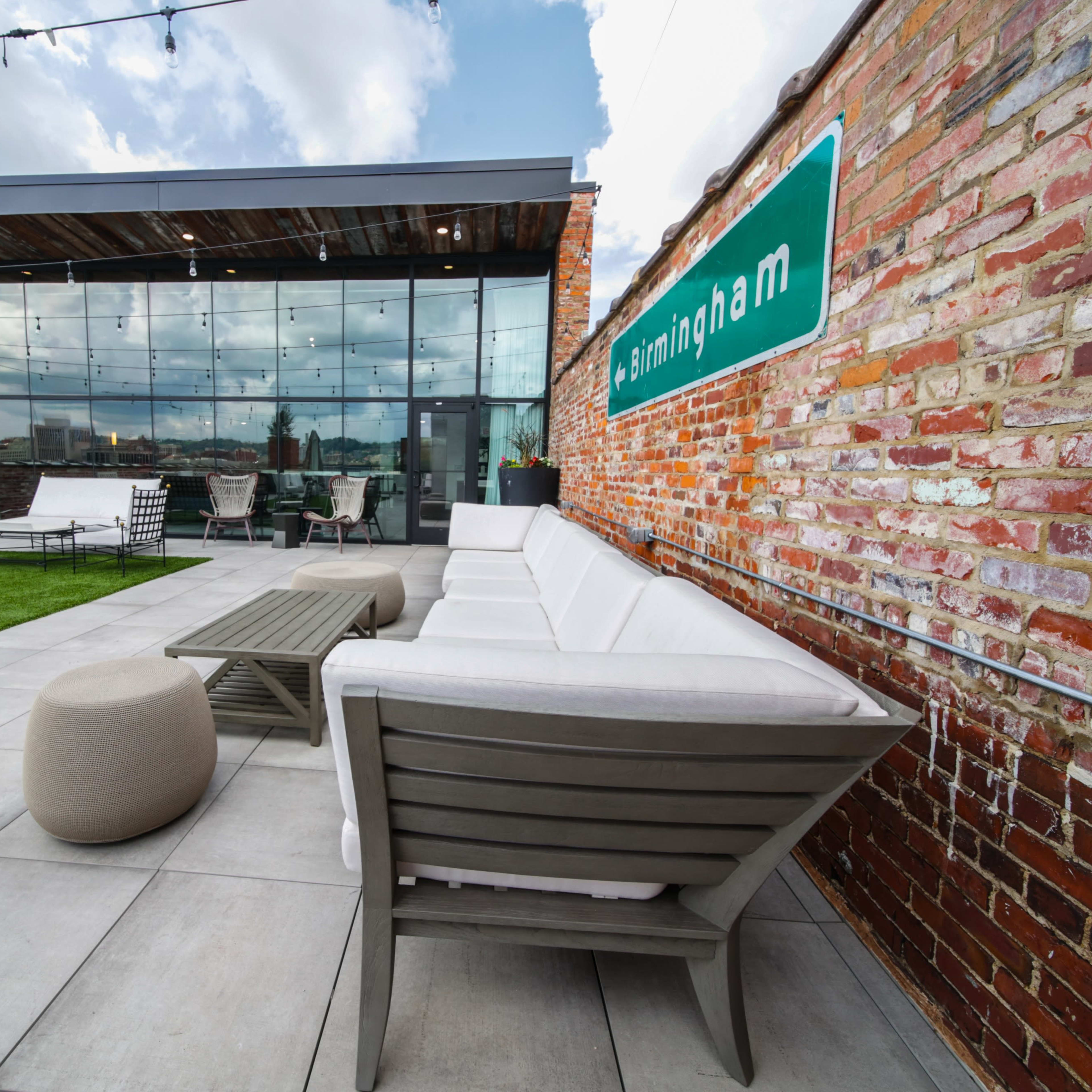 A modern rooftop terrace with comfortable seating, a grassy area, and large glass windows overlooking a cityscape.