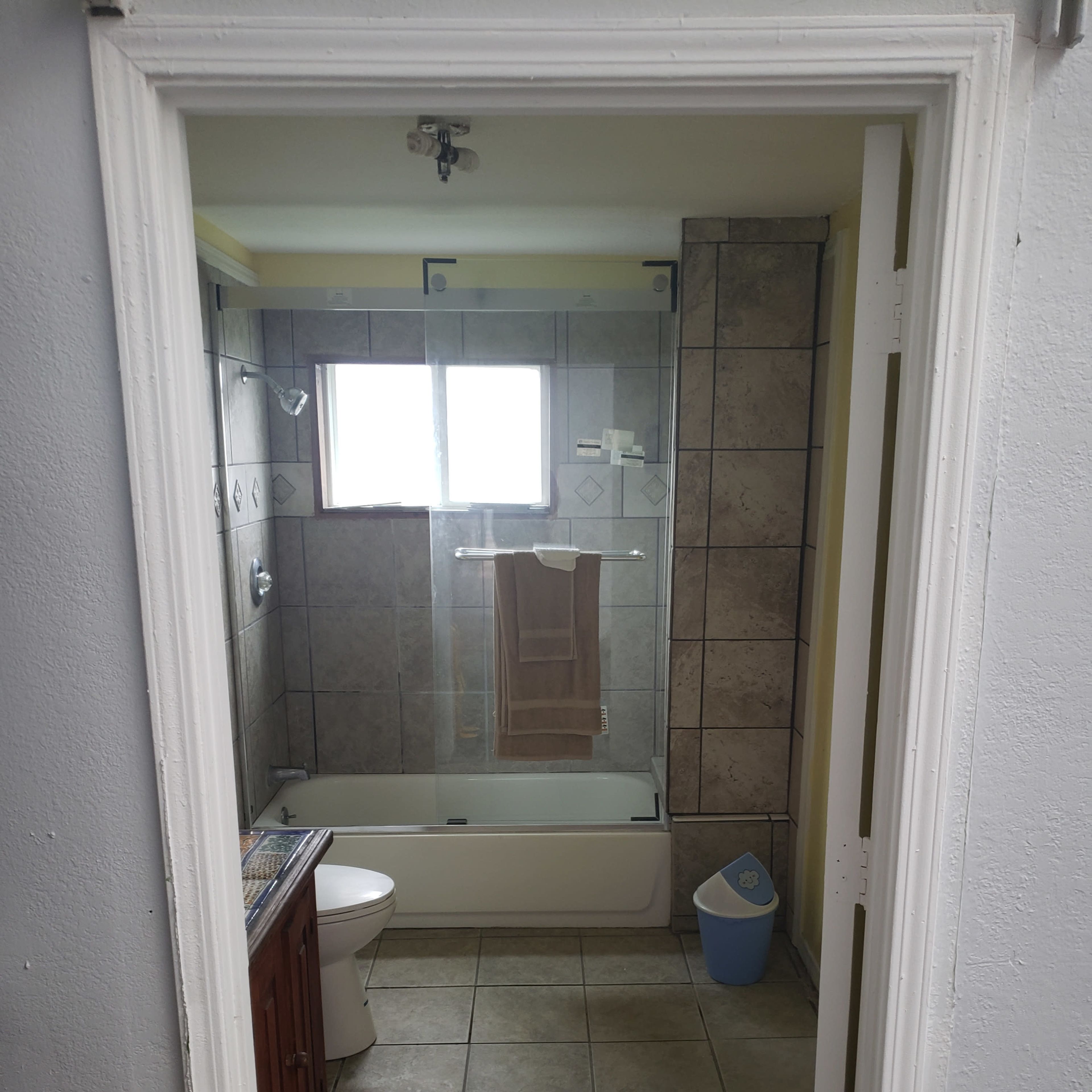 A bathroom with a bathtub, toilet, and a window, featuring tiled walls and a small wooden cabinet.