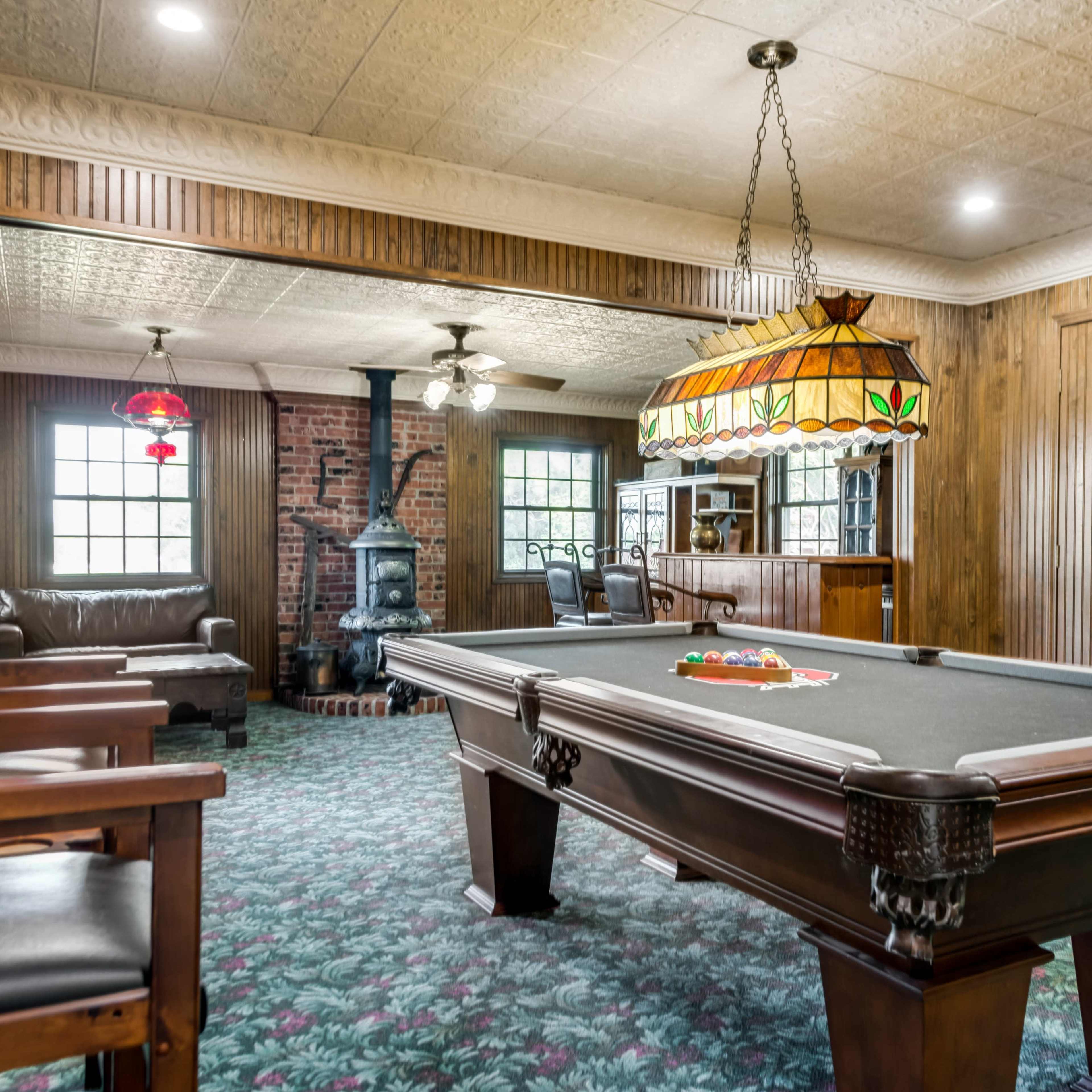 A spacious game room featuring a billiard table, a fireplace, wooden paneling, and a cozy seating area with a sofa.