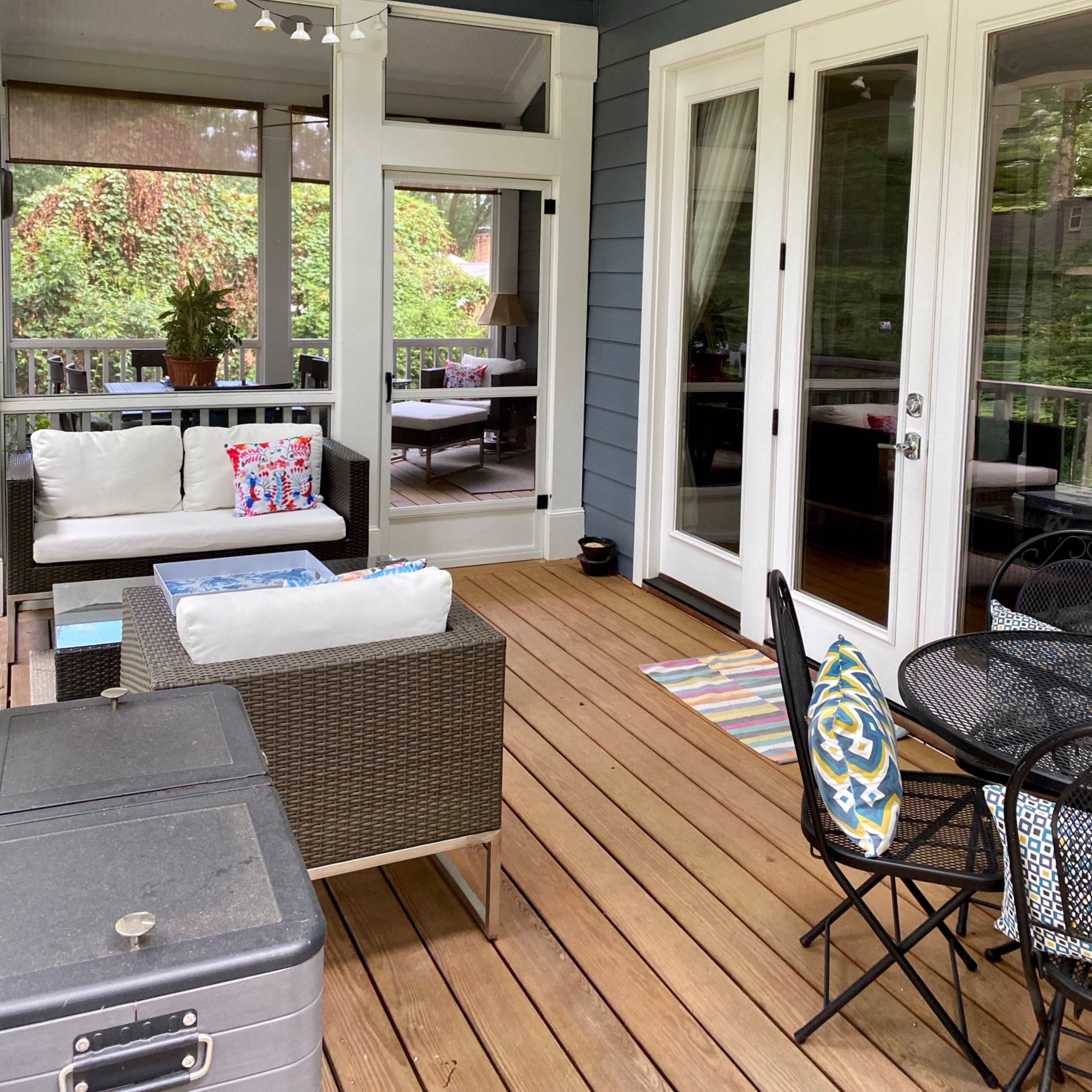 A screened porch with seating, a ceiling fan, and wooden flooring, surrounded by greenery.