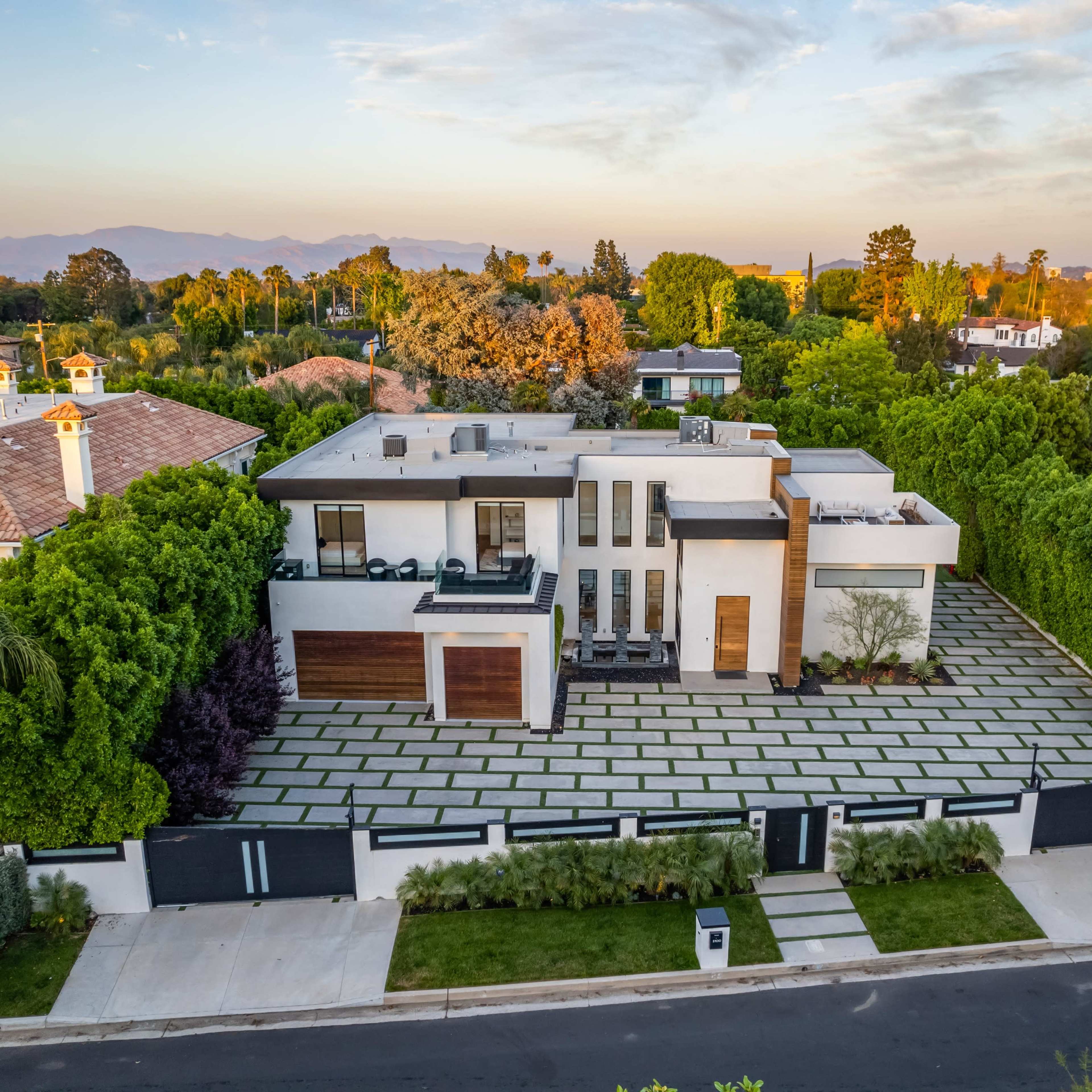 A modern house with a flat roof, surrounded by lush greenery and a stone-paved driveway.