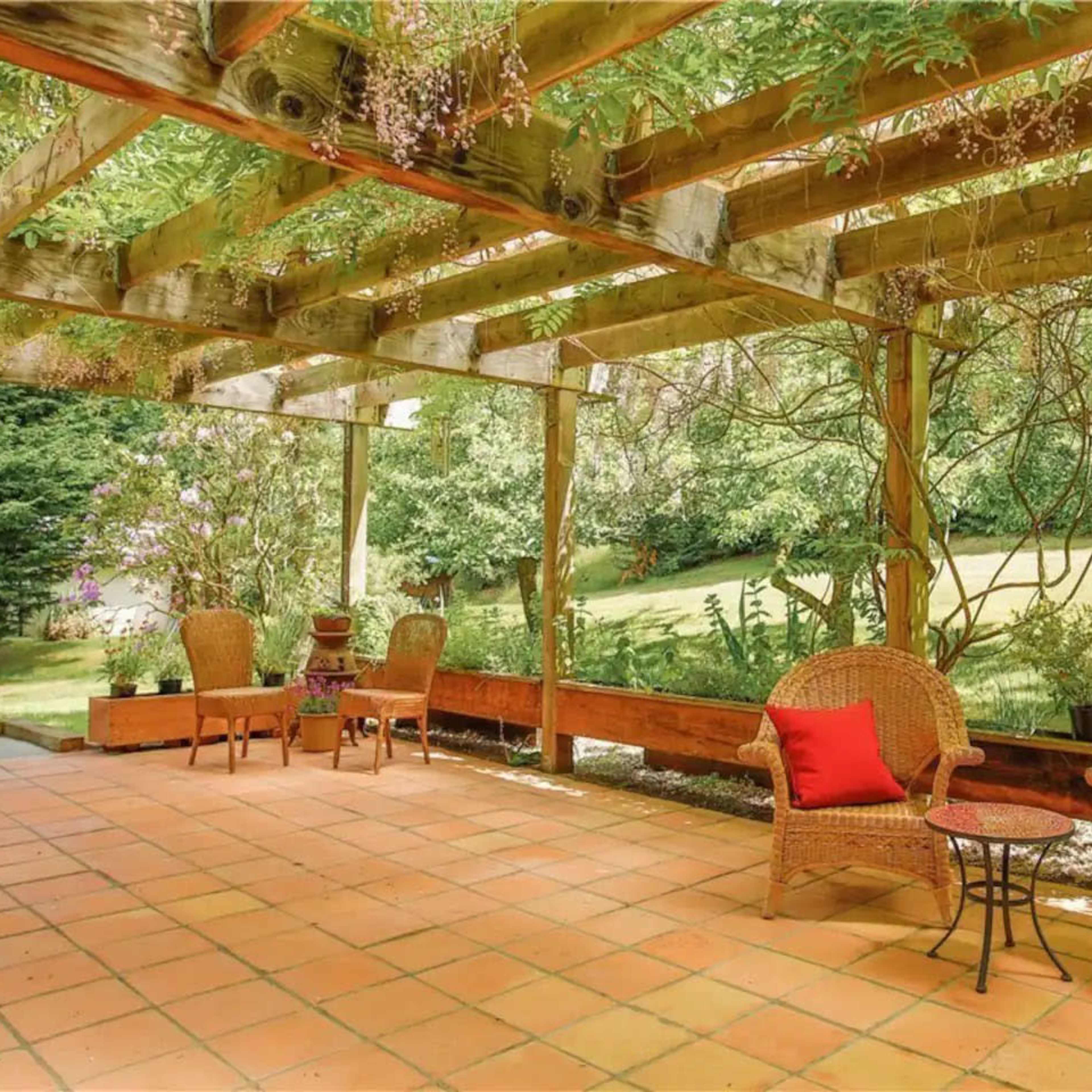 A patio area with wicker furniture and red cushions under a wooden pergola adorned with greenery.