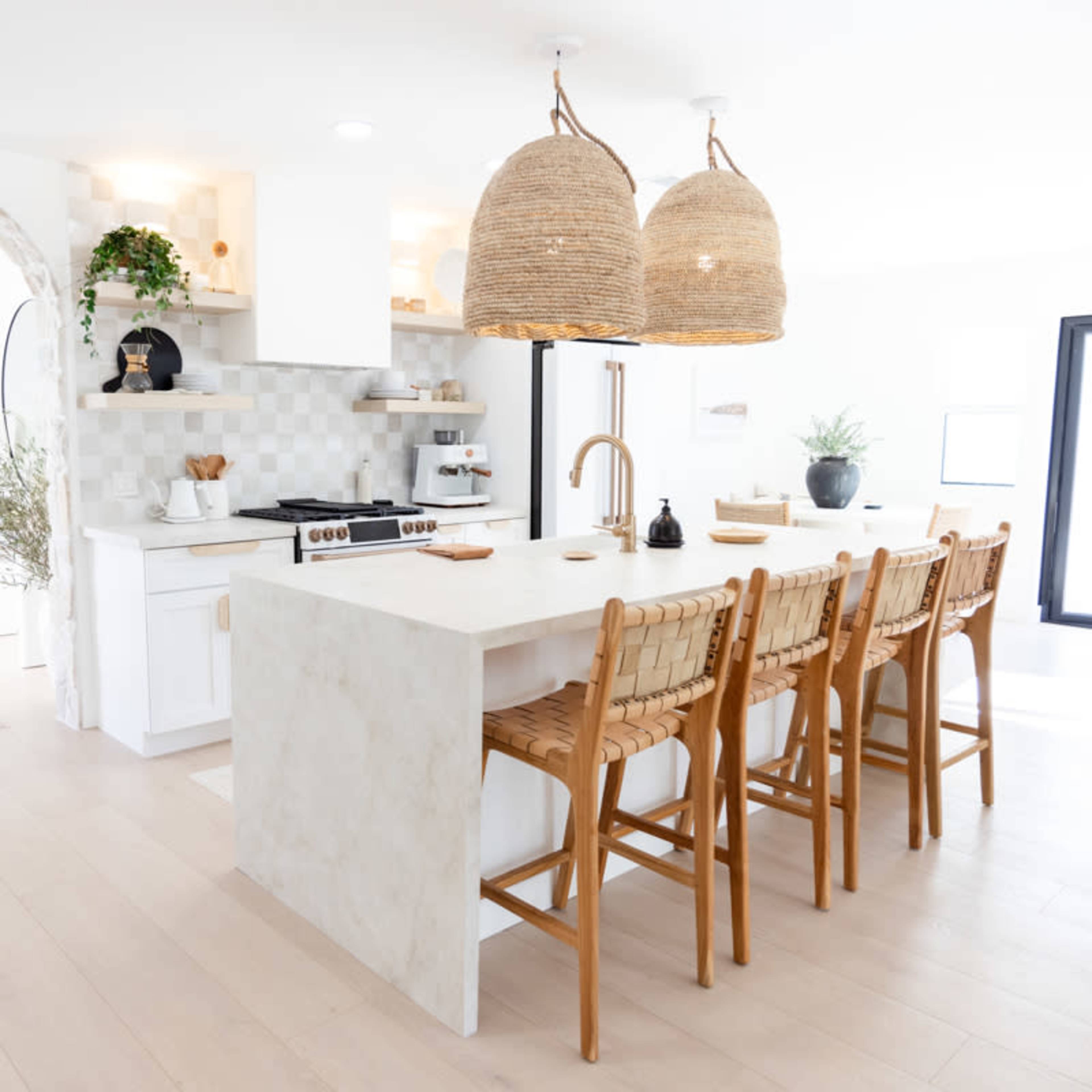 A modern kitchen features a large island with bar seating, white cabinetry, and two woven pendant lights.
