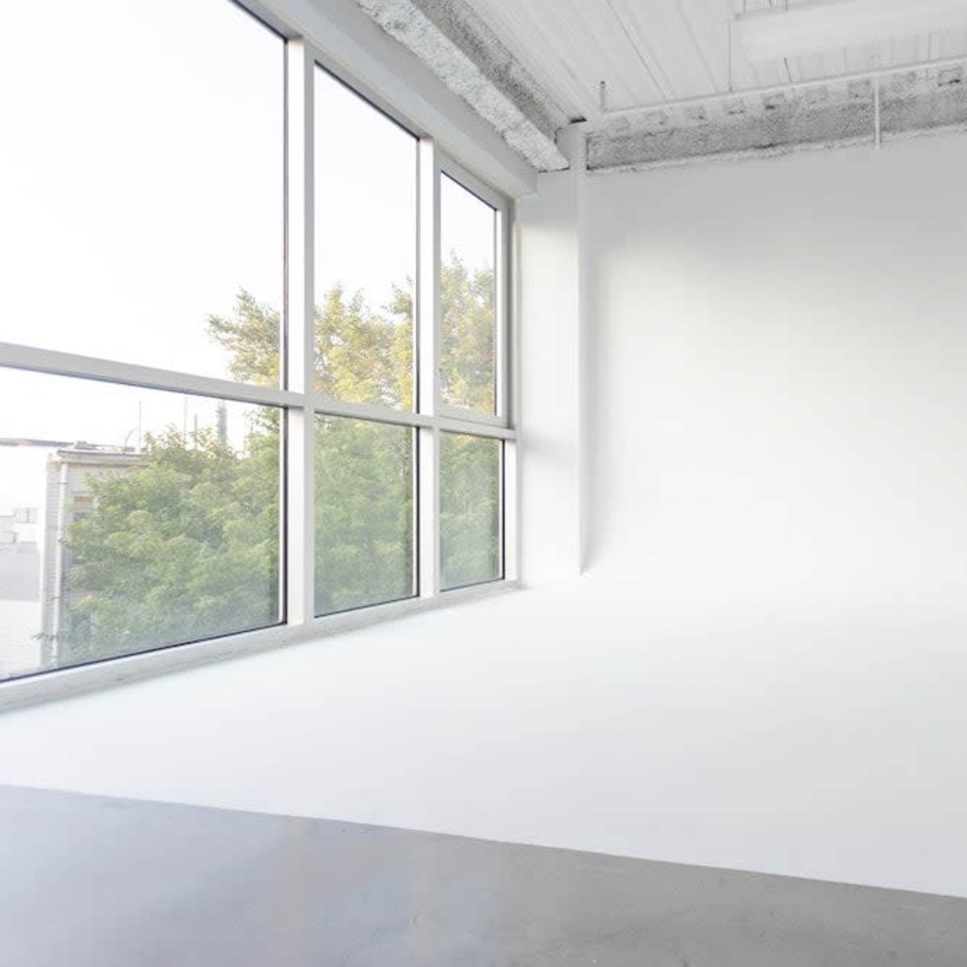 A spacious, empty room with large windows letting in natural light and a seamless white backdrop.