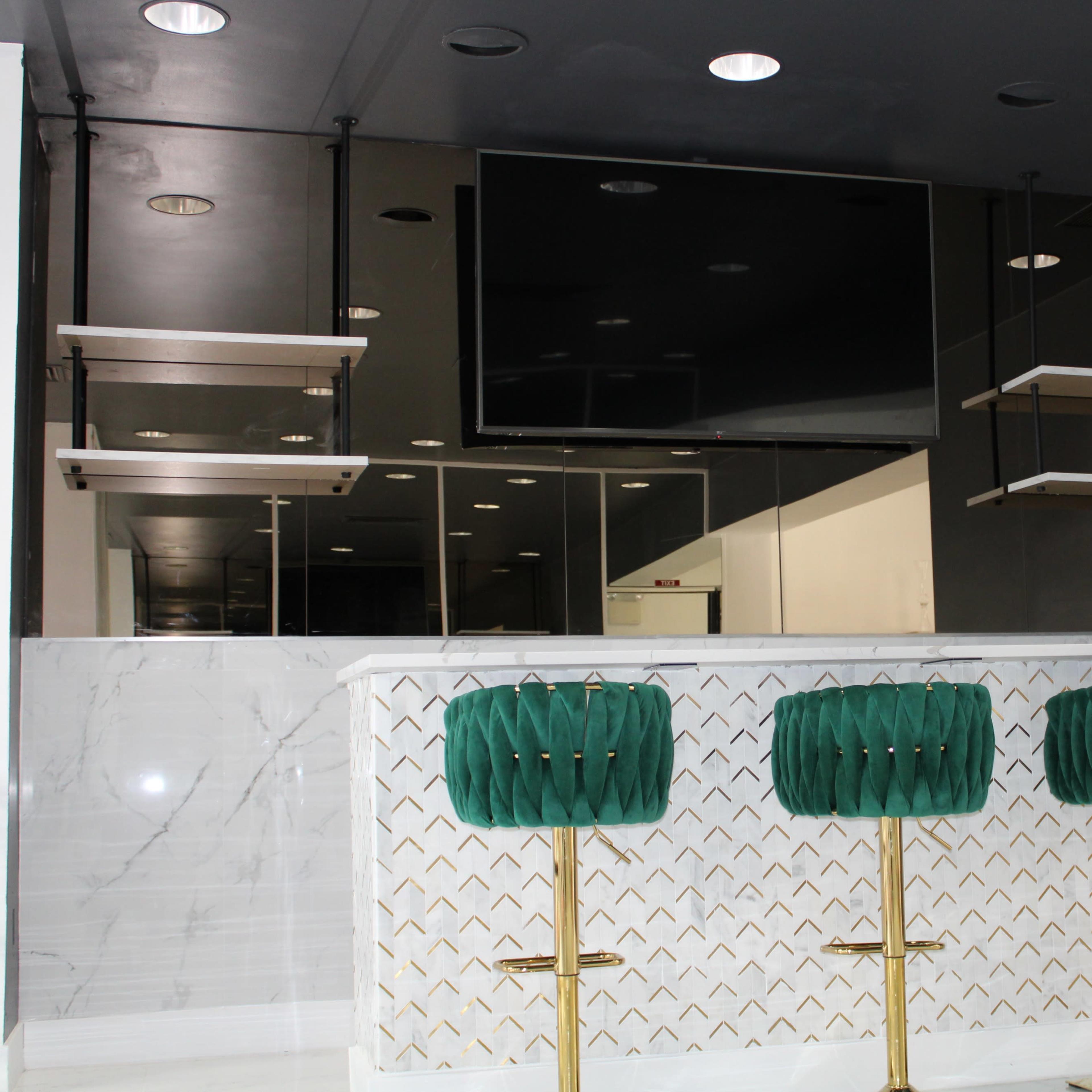 A modern bar area with three green bar stools, a marble counter, and floating shelves against a dark wall.