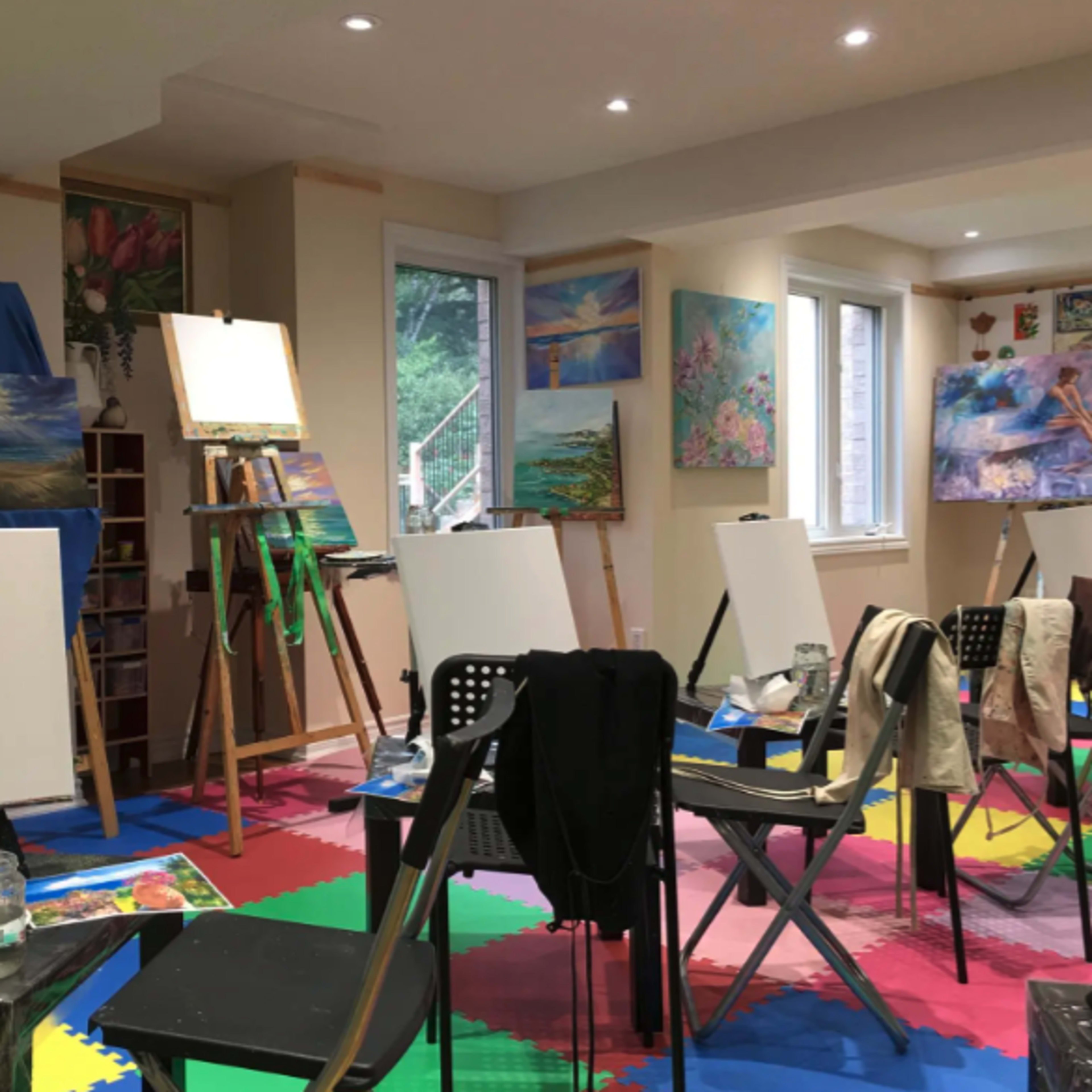 An art studio with empty canvases on easels, scattered art supplies on tables, and colorful artwork displayed on the walls.