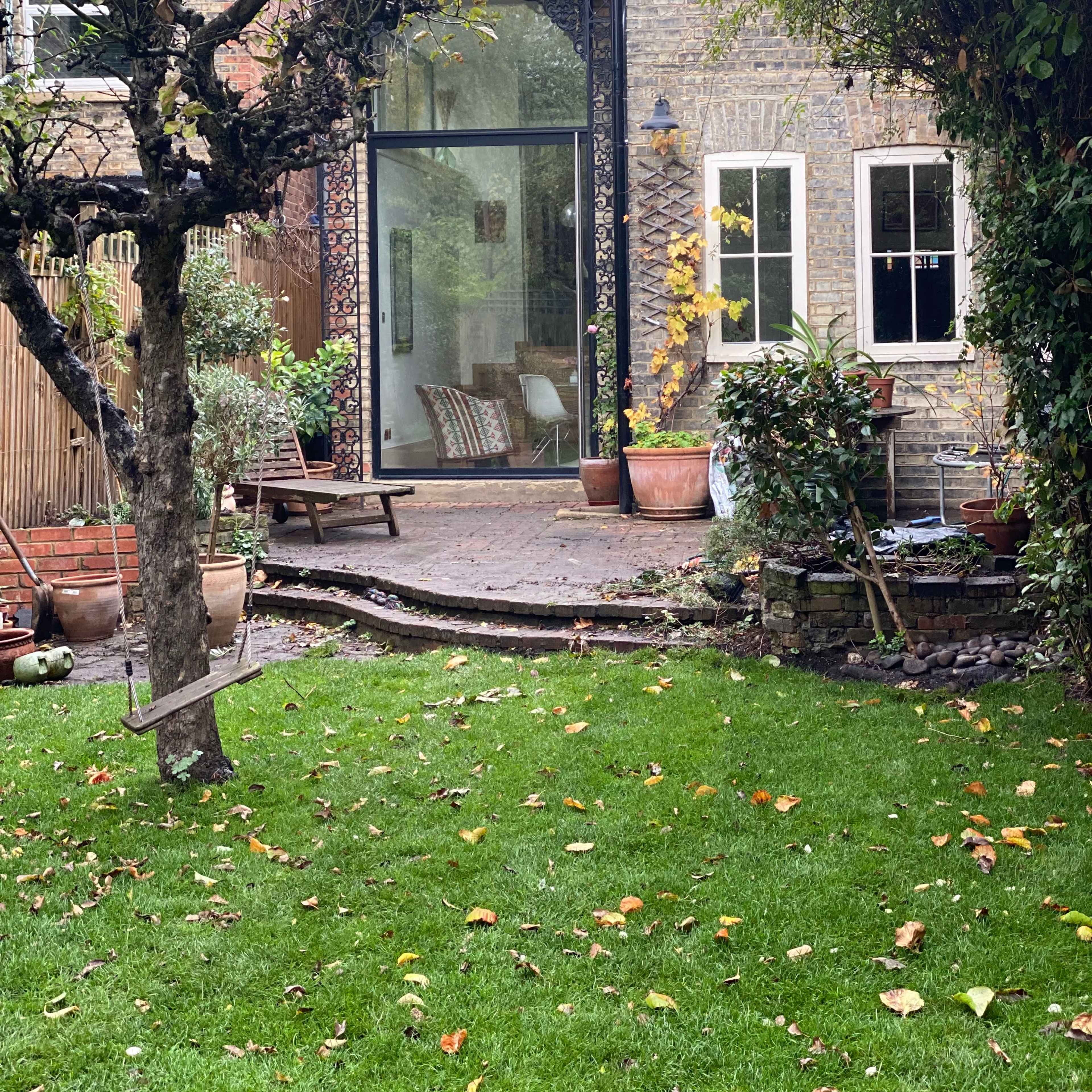 A brick house features a large glass door opening to a garden with a tree and various potted plants.