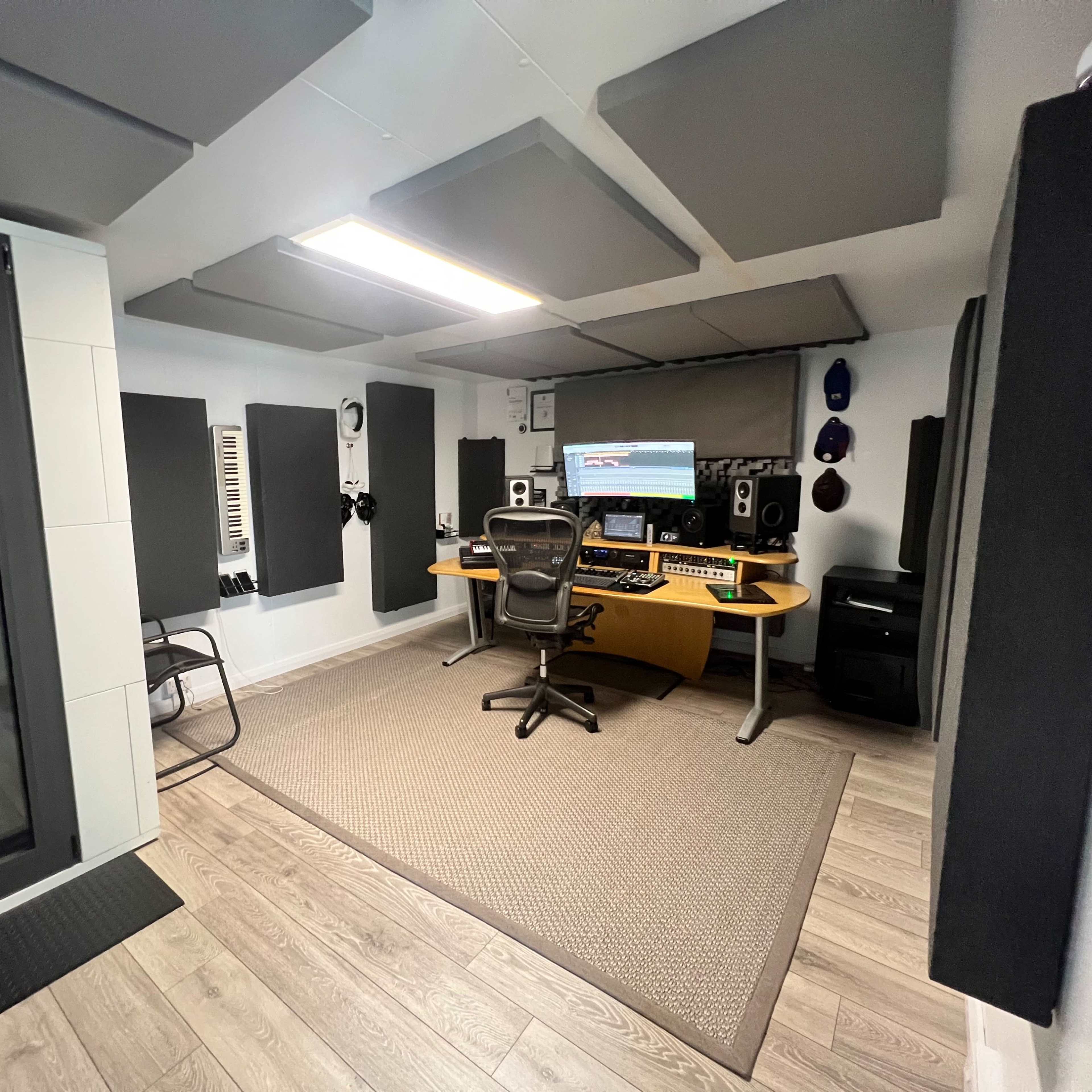 A modern music studio featuring a computer workstation, soundproof panels on the walls, and a glass isolation booth.