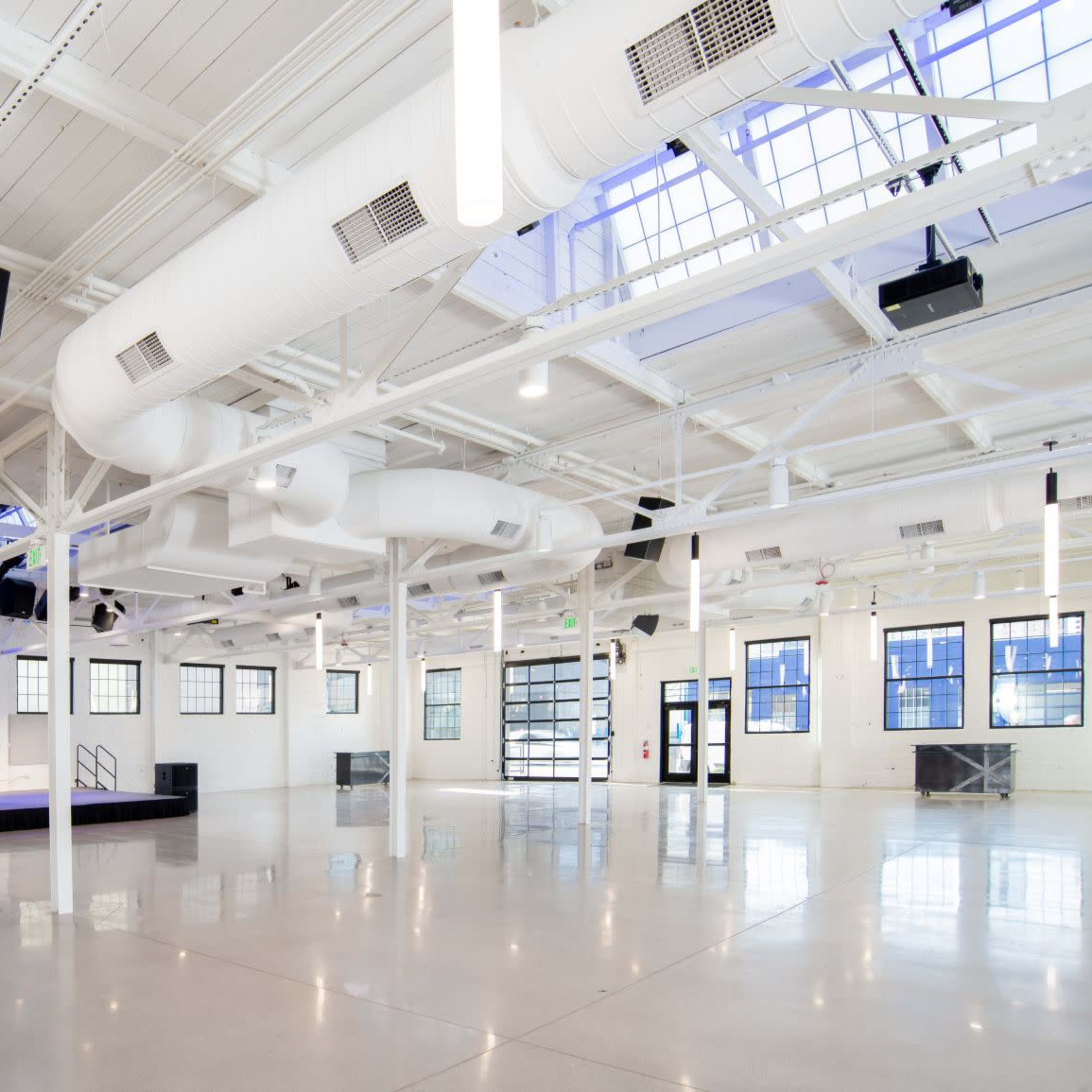 A spacious, modern event venue with high ceilings, large windows, and exposed ductwork.