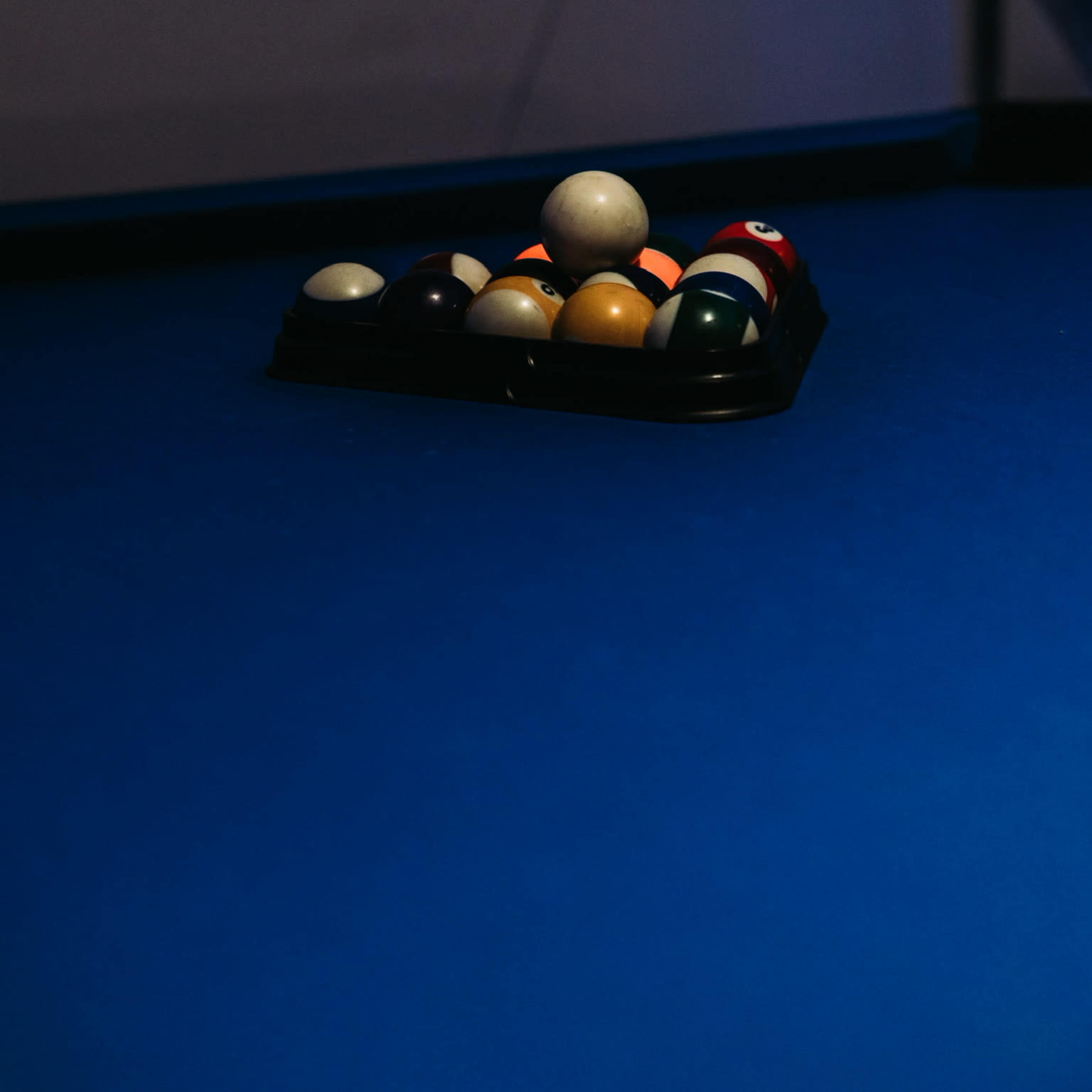 A triangular rack of billiard balls sits on a blue pool table.