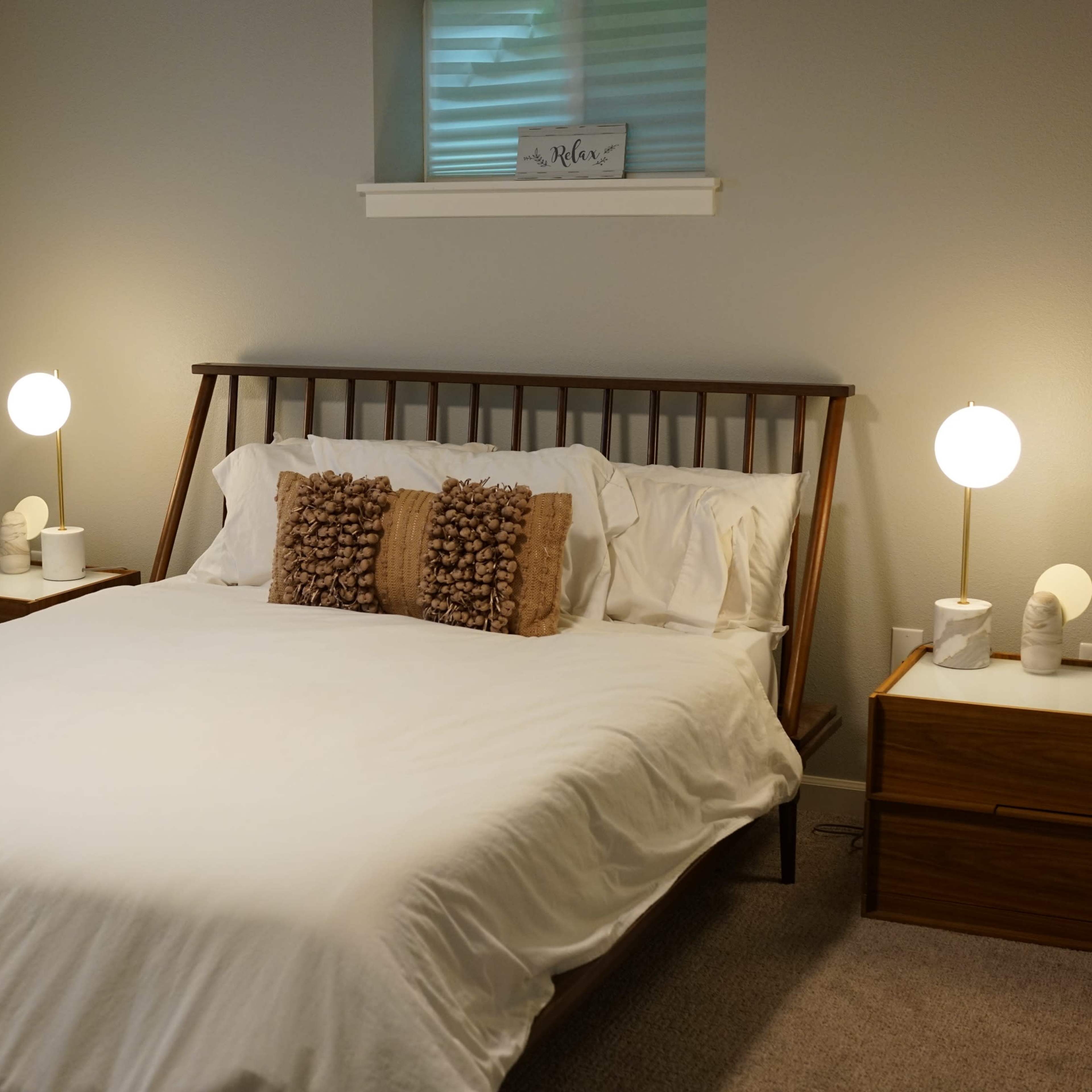 A minimalist bedroom features a bed with white bedding, flanked by two wooden nightstands with lamps.