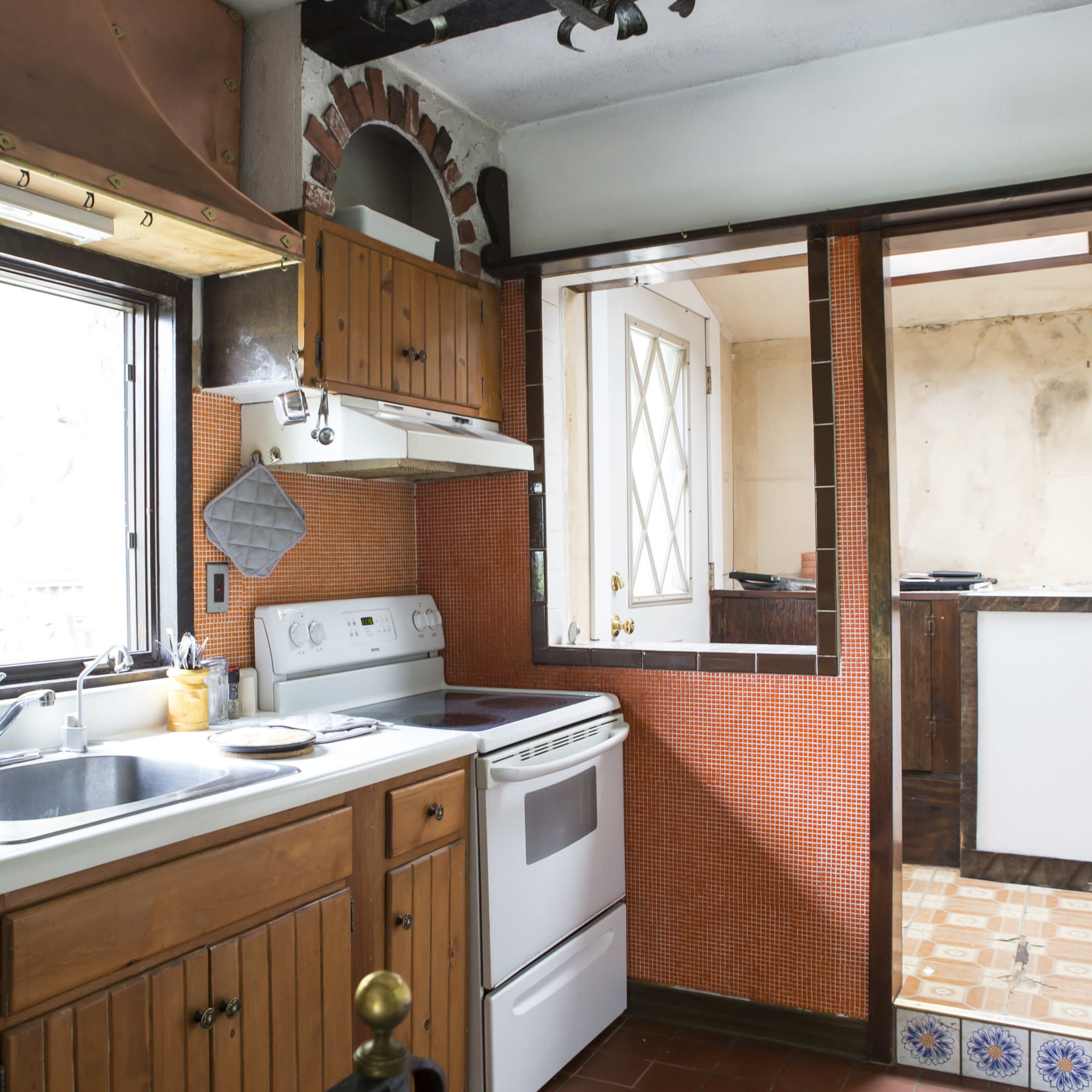 A kitchen with wooden cabinets, a sink, a stove, and a door leading to another room.