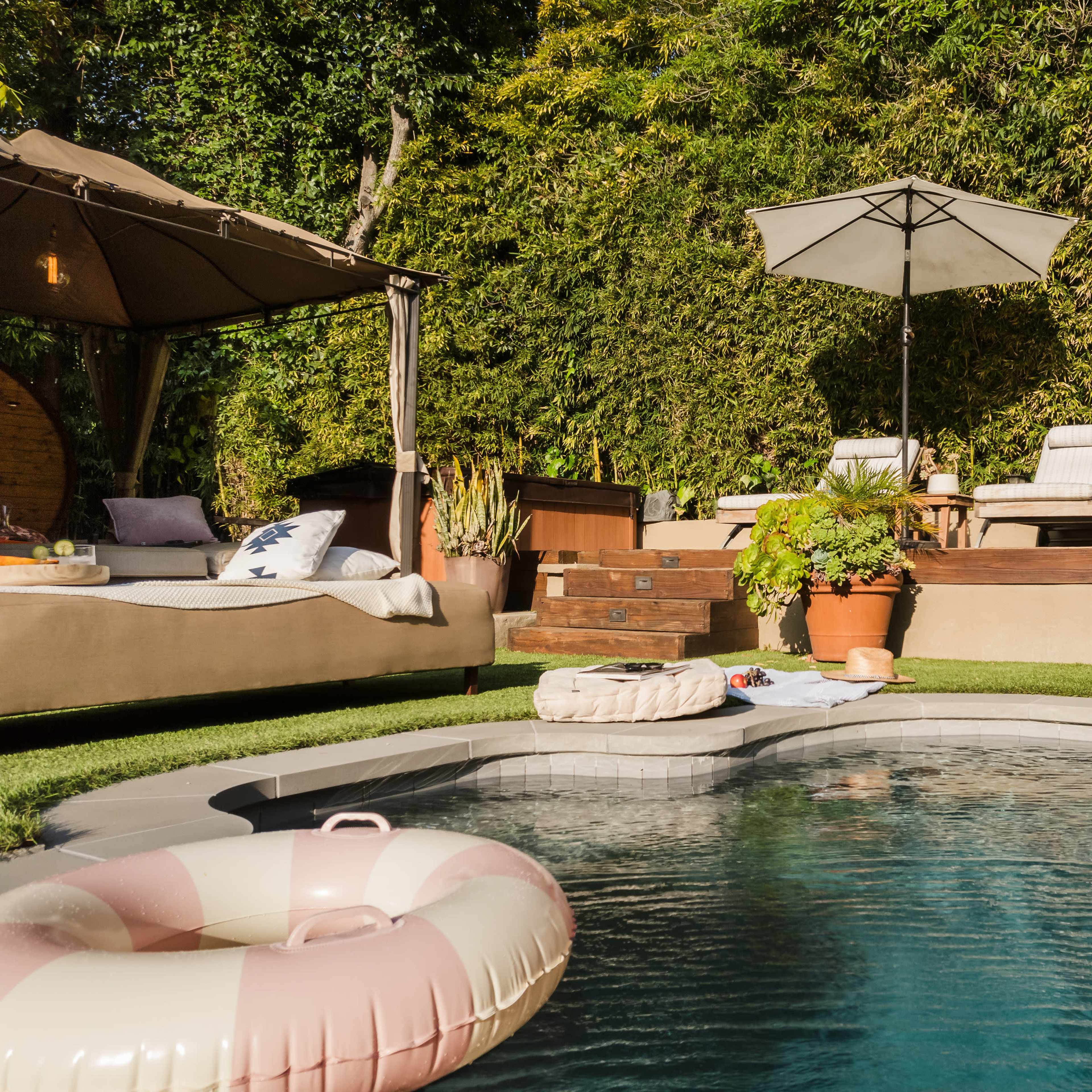 A swimming pool surrounded by lounge chairs, umbrellas, and a gazebo, with a cozy area for relaxation and lush greenery in the background.