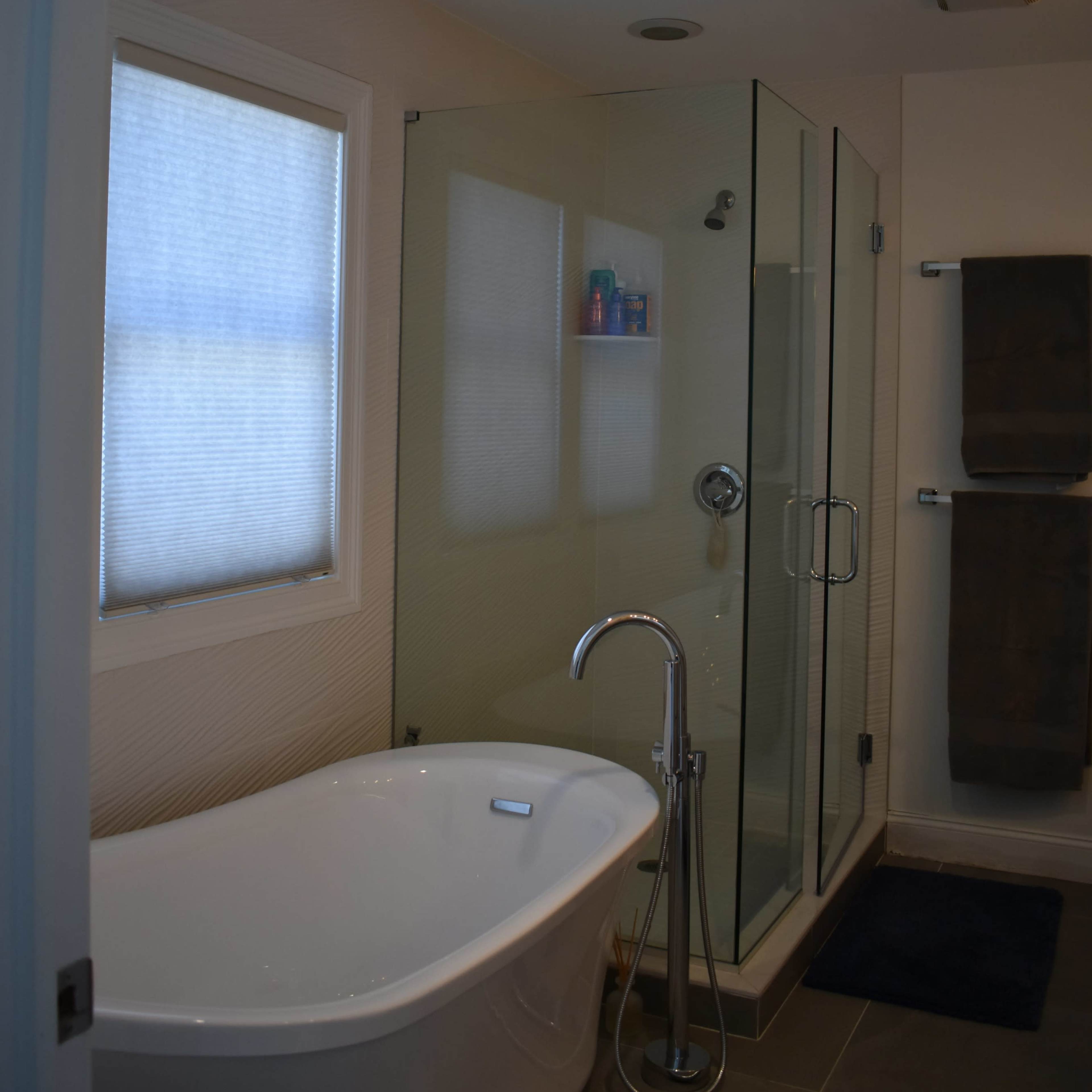 A modern bathroom featuring a freestanding bathtub, a glass shower enclosure, and a towel rack with two towels.