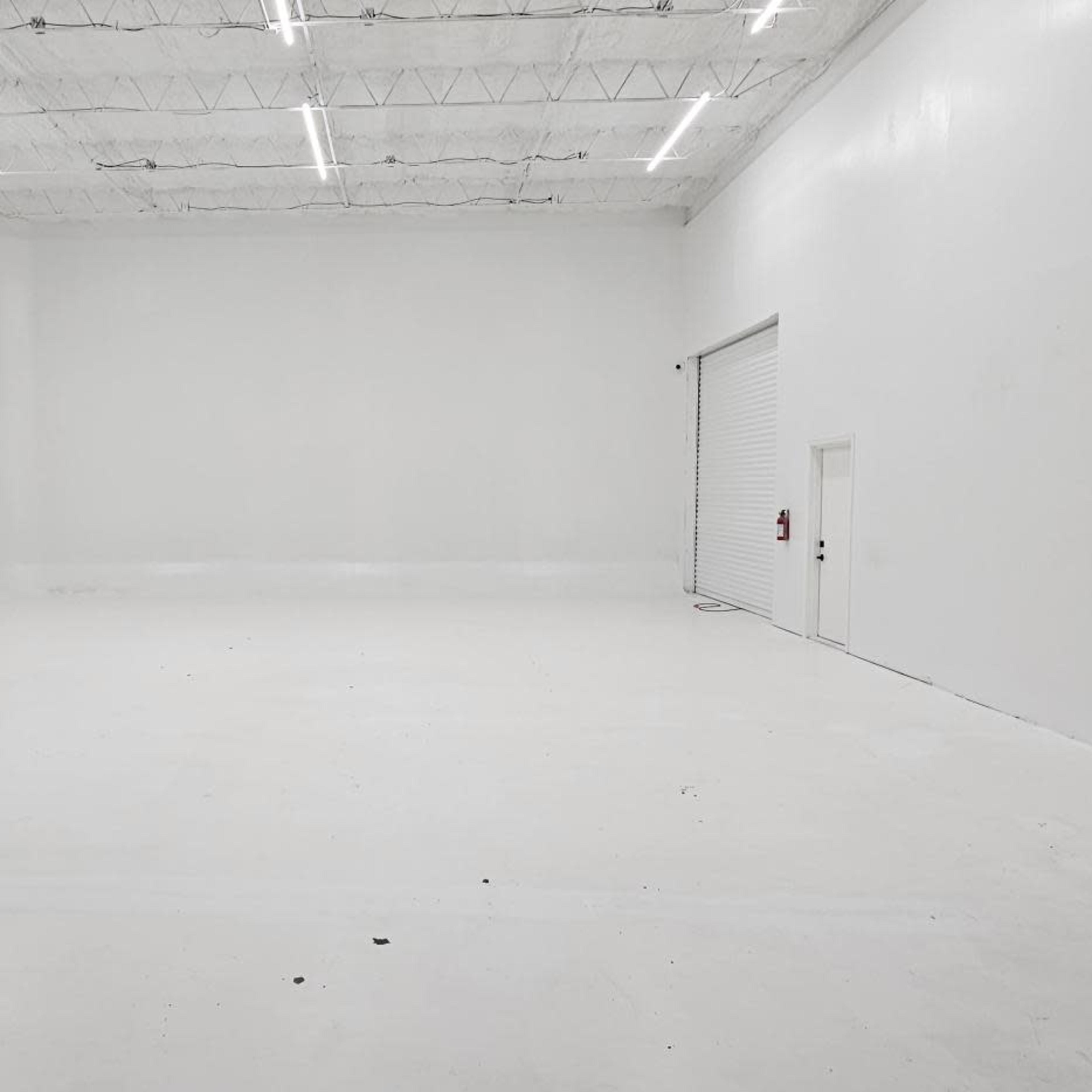 A large, empty white room with high ceilings and a door on one side.