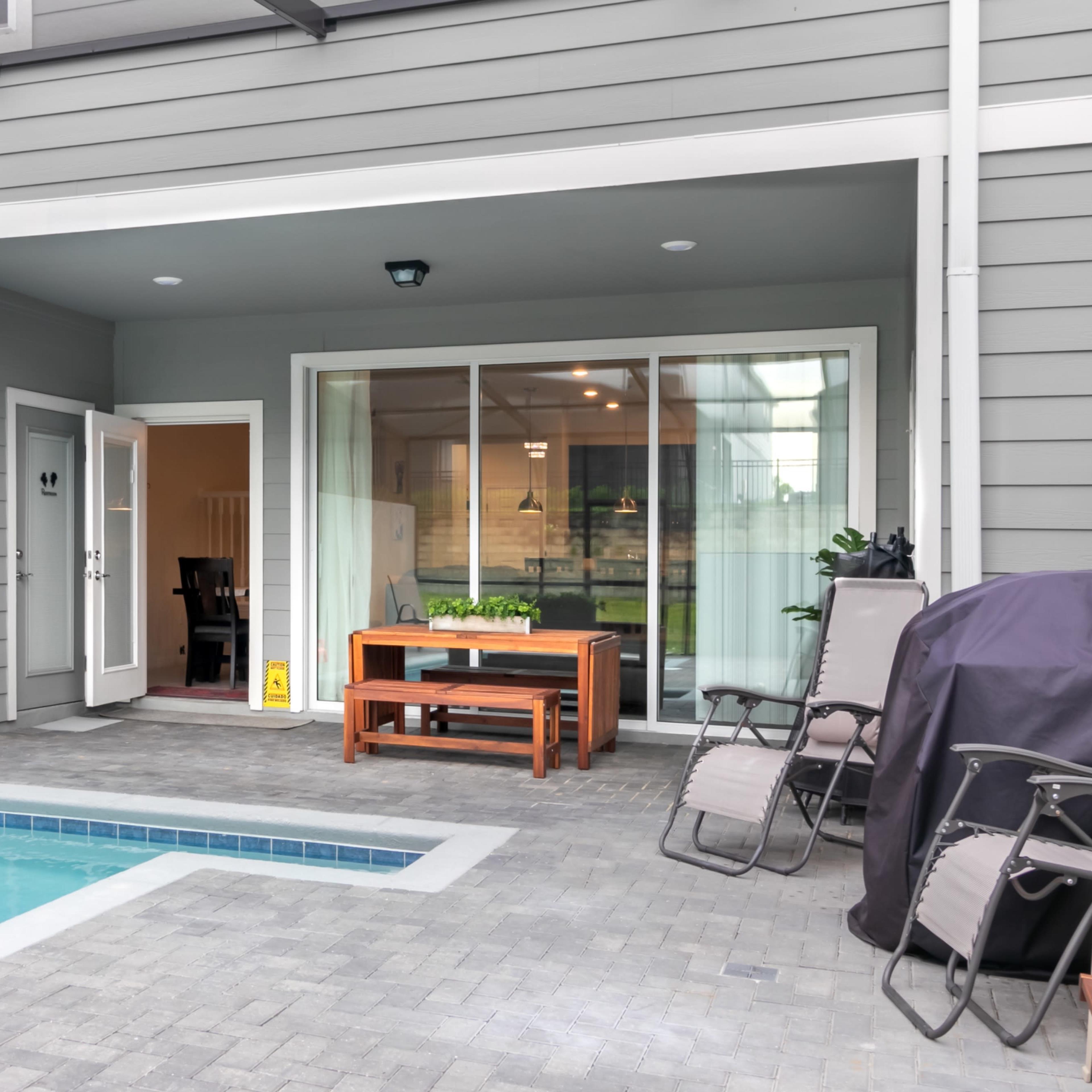 A modern patio area featuring a small swimming pool, outdoor furniture, and large sliding glass doors leading into an indoor space.