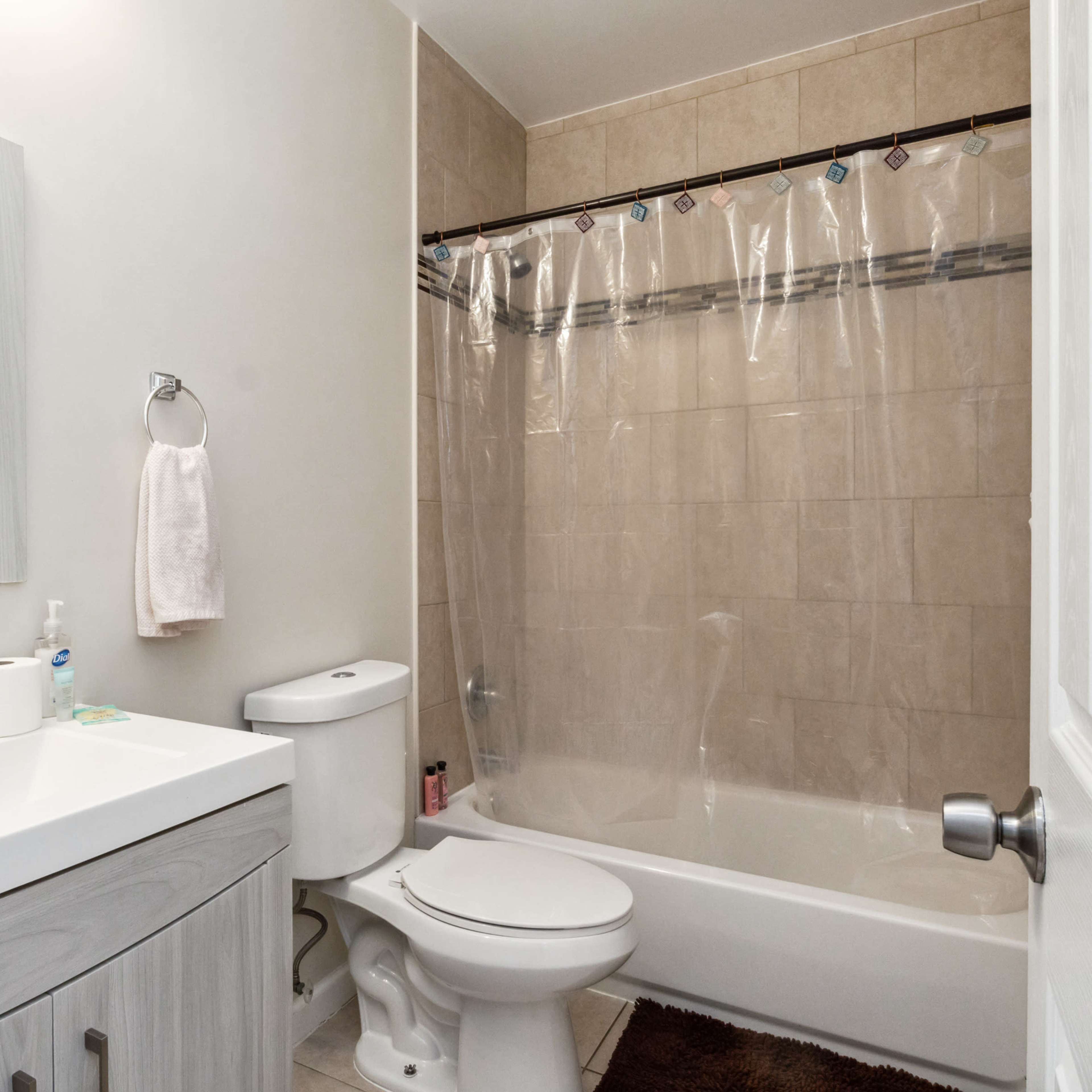A bathroom with a bathtub and shower combination, a toilet, a sink with a mirror above it, and tiled walls.