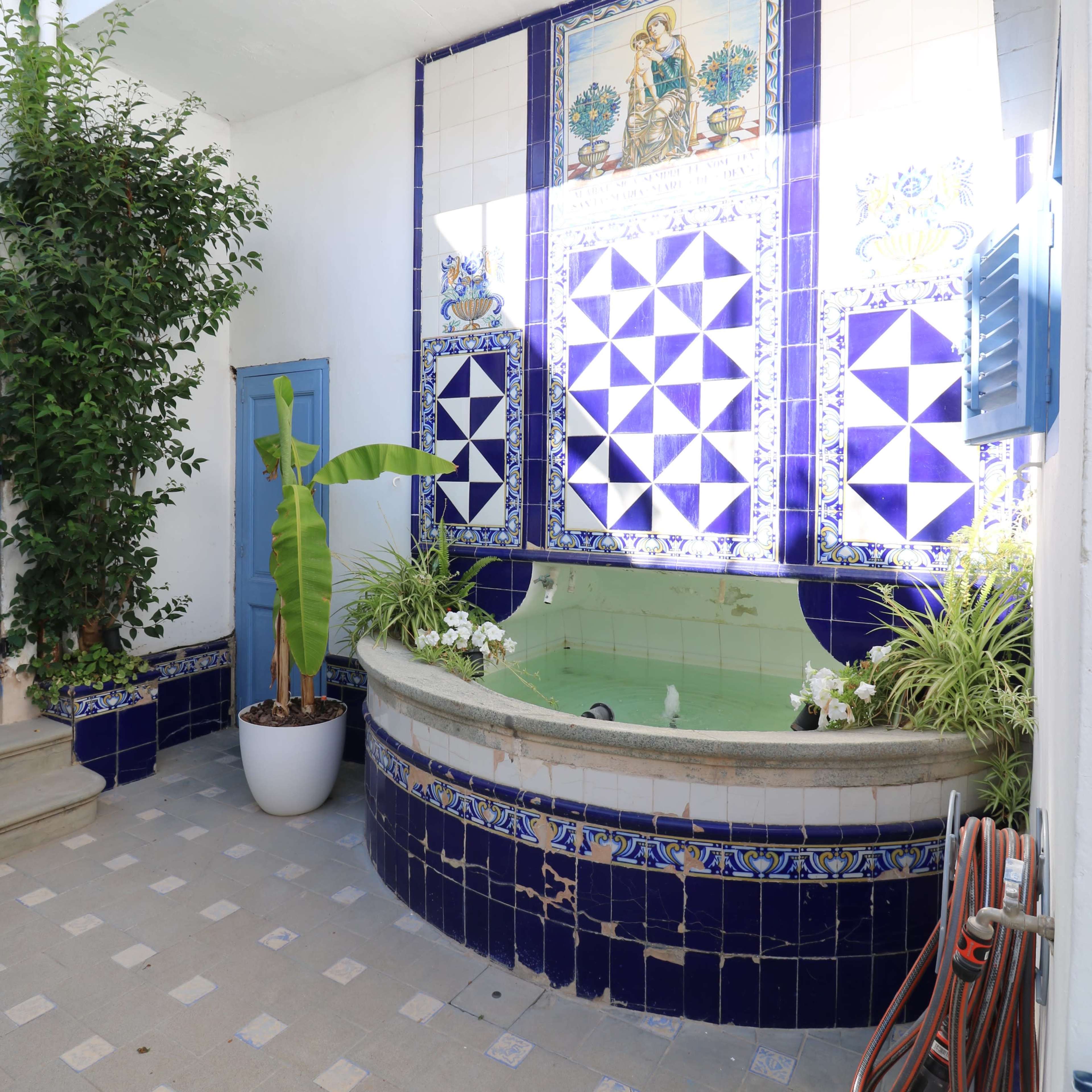 A tiled courtyard with a circular fountain surrounded by greenery and decorative tiles.