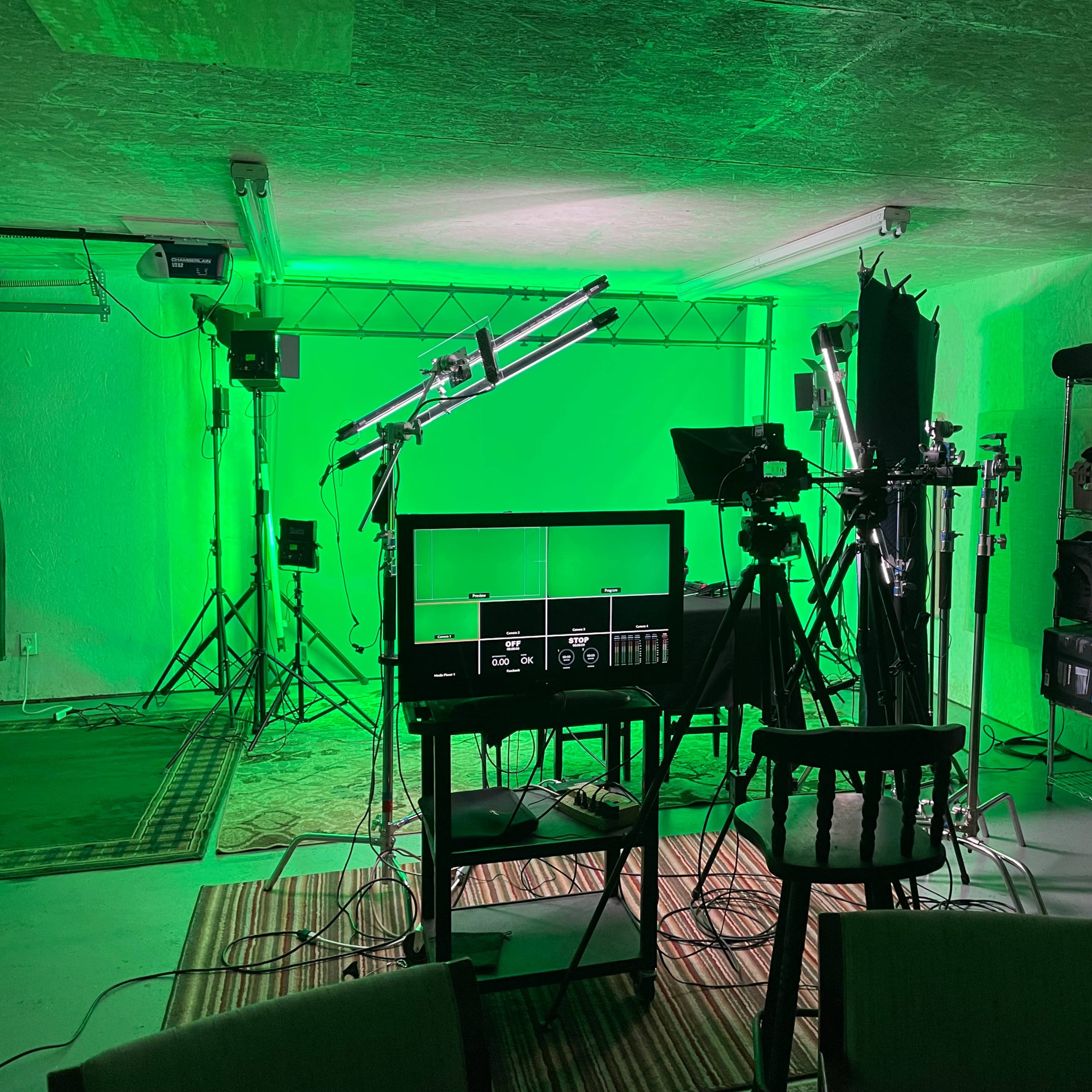 A green-lit studio setup with camera equipment, lighting rigs, and various props arranged in a spacious room.