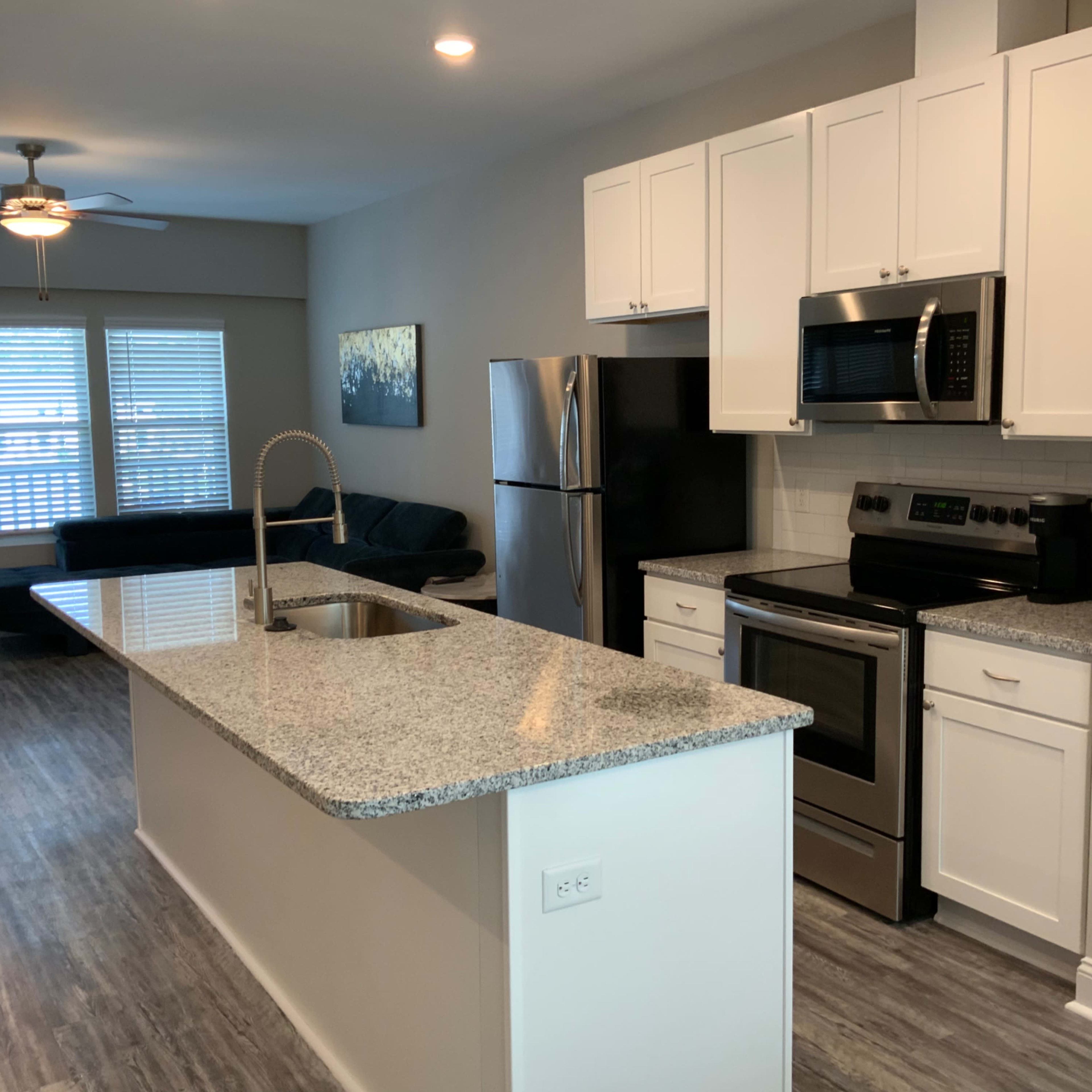 A modern kitchen with white cabinets, stainless steel appliances, and a granite countertop island.