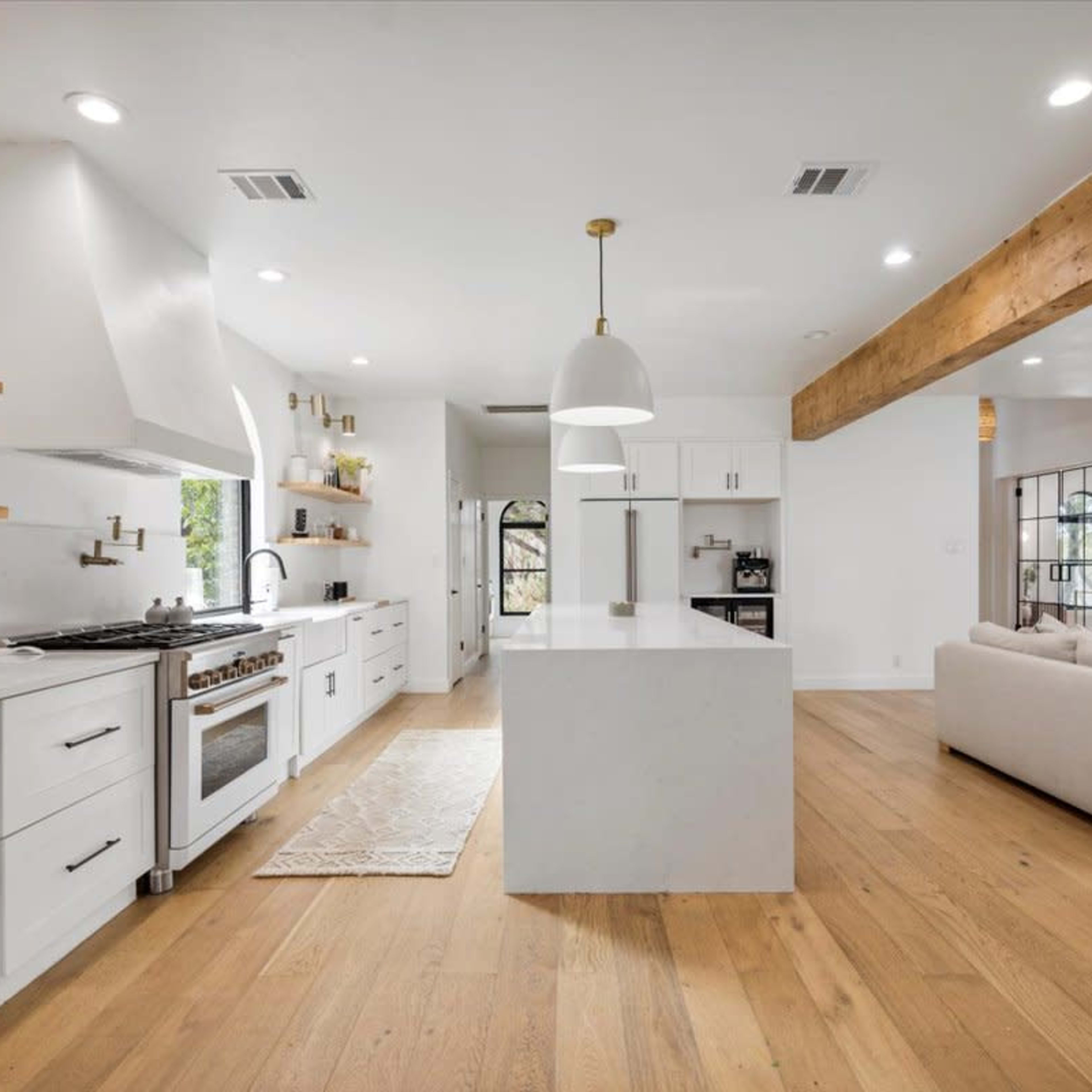 A modern kitchen with white cabinetry, a central island, and an open layout that connects to a living area with a beige sofa.