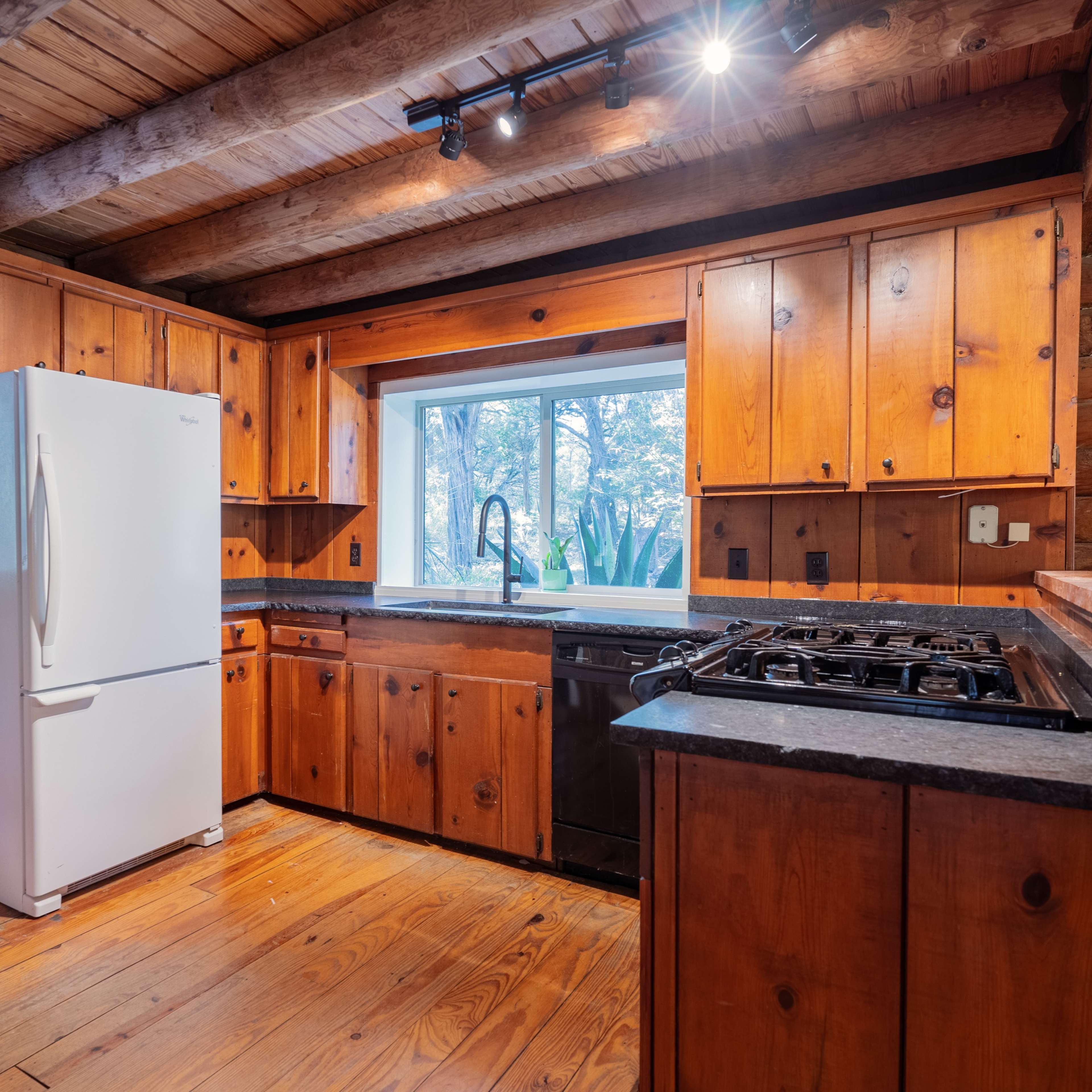 The kitchen features wooden cabinetry, a white refrigerator, and a gas stove, with a window that overlooks a natural setting.
